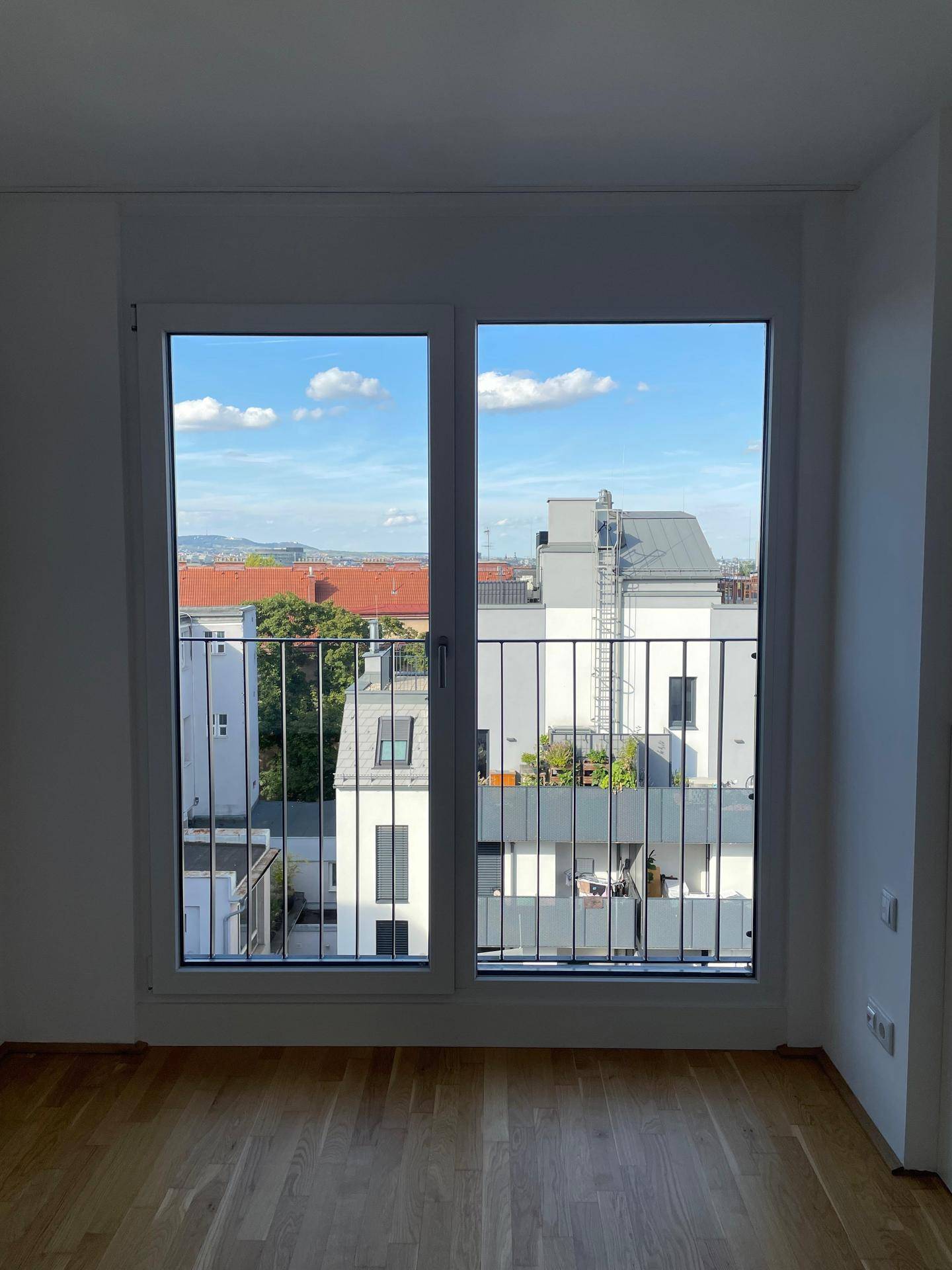 Große Fensterfront mit französischem Balkon und Blick auf die Nachbarschaft und den blauen Himmel.
