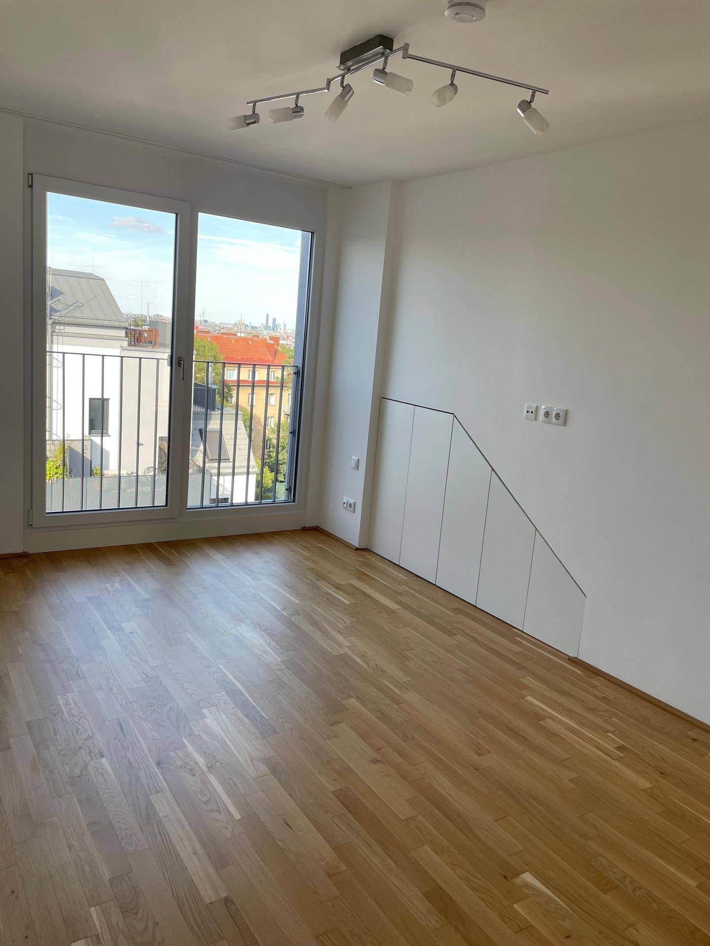 Geräumiger Raum mit Holzboden, Einbauschränken und französischem Balkon für viel Tageslicht.