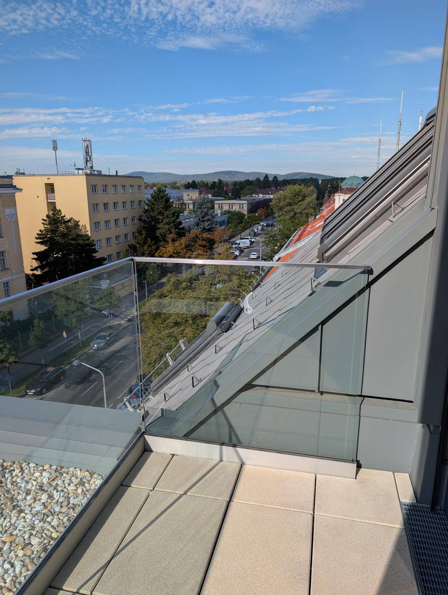 Balkon mit Glasgeländer und Blick auf die Straße sowie die umliegende Bebauung der Stadt.