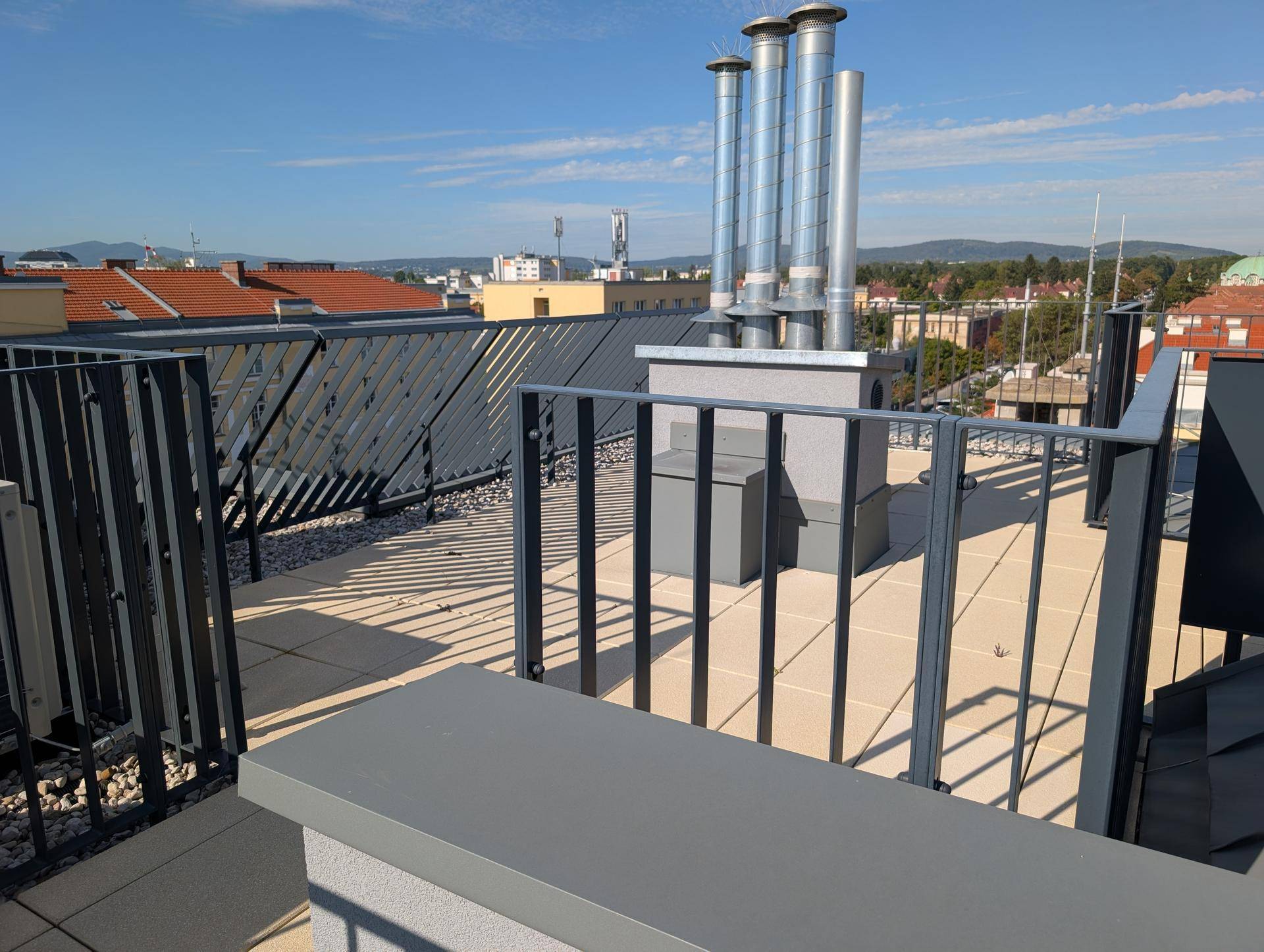 Dachterrasse mit modernen Metallgeländern und Blick auf die umliegenden Gebäude unter klarem Himmel.