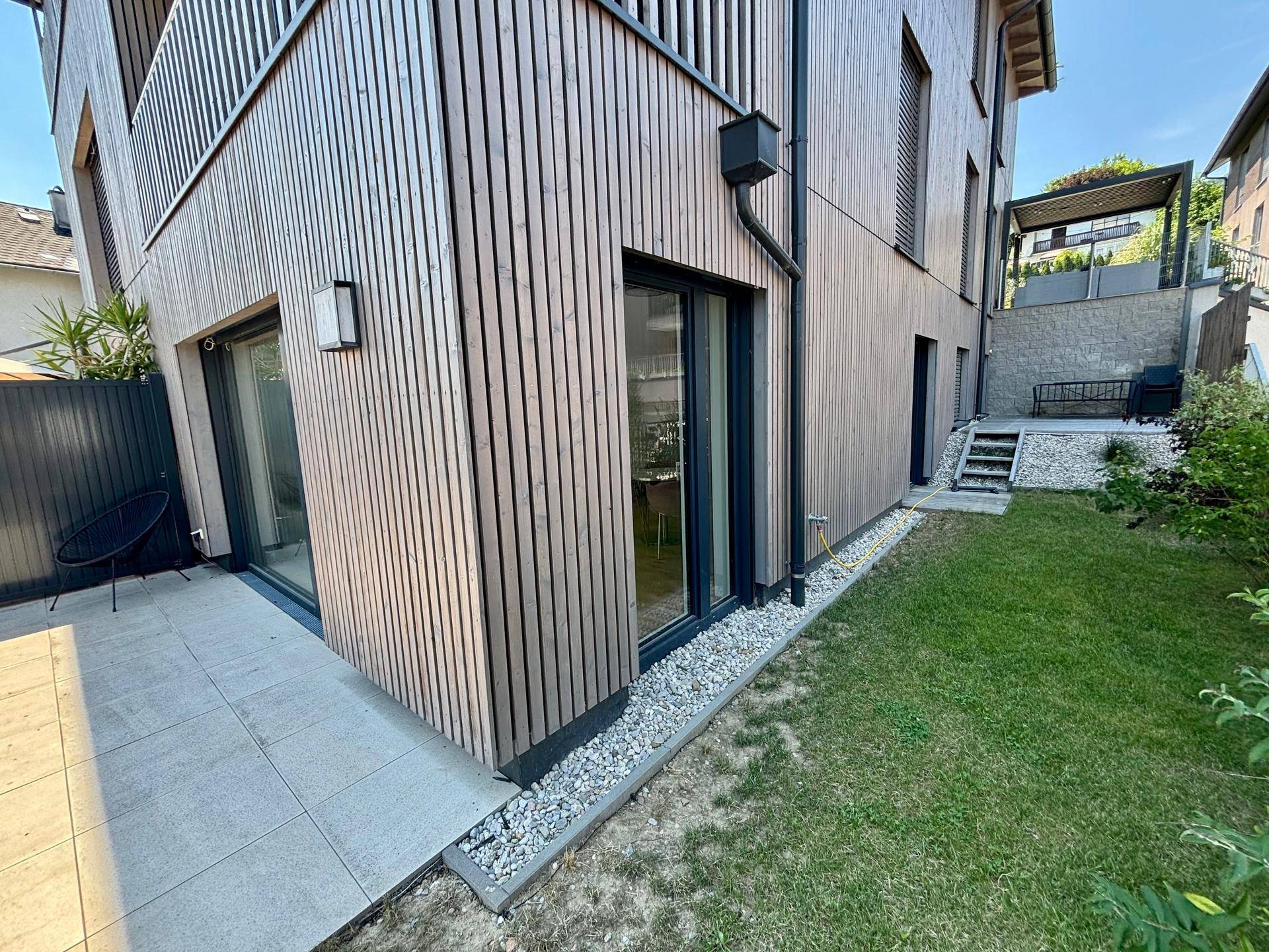 Seitlicher Gartenbereich mit kleiner Terrasse und moderner Holzfassade des Hauses.
