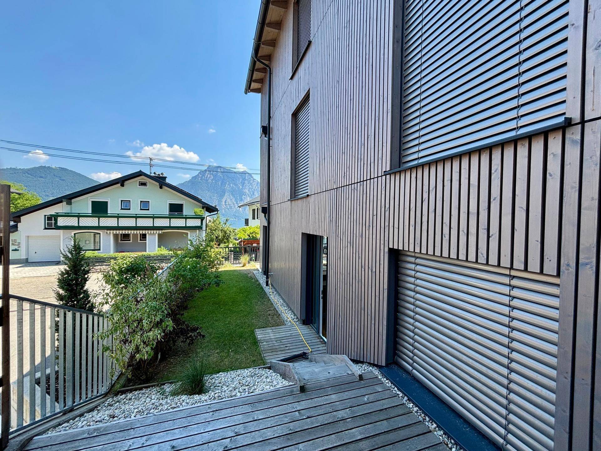 Moderne Holzfassade des Gebäudes mit Außenjalousien und Bergblick im Hintergrund.