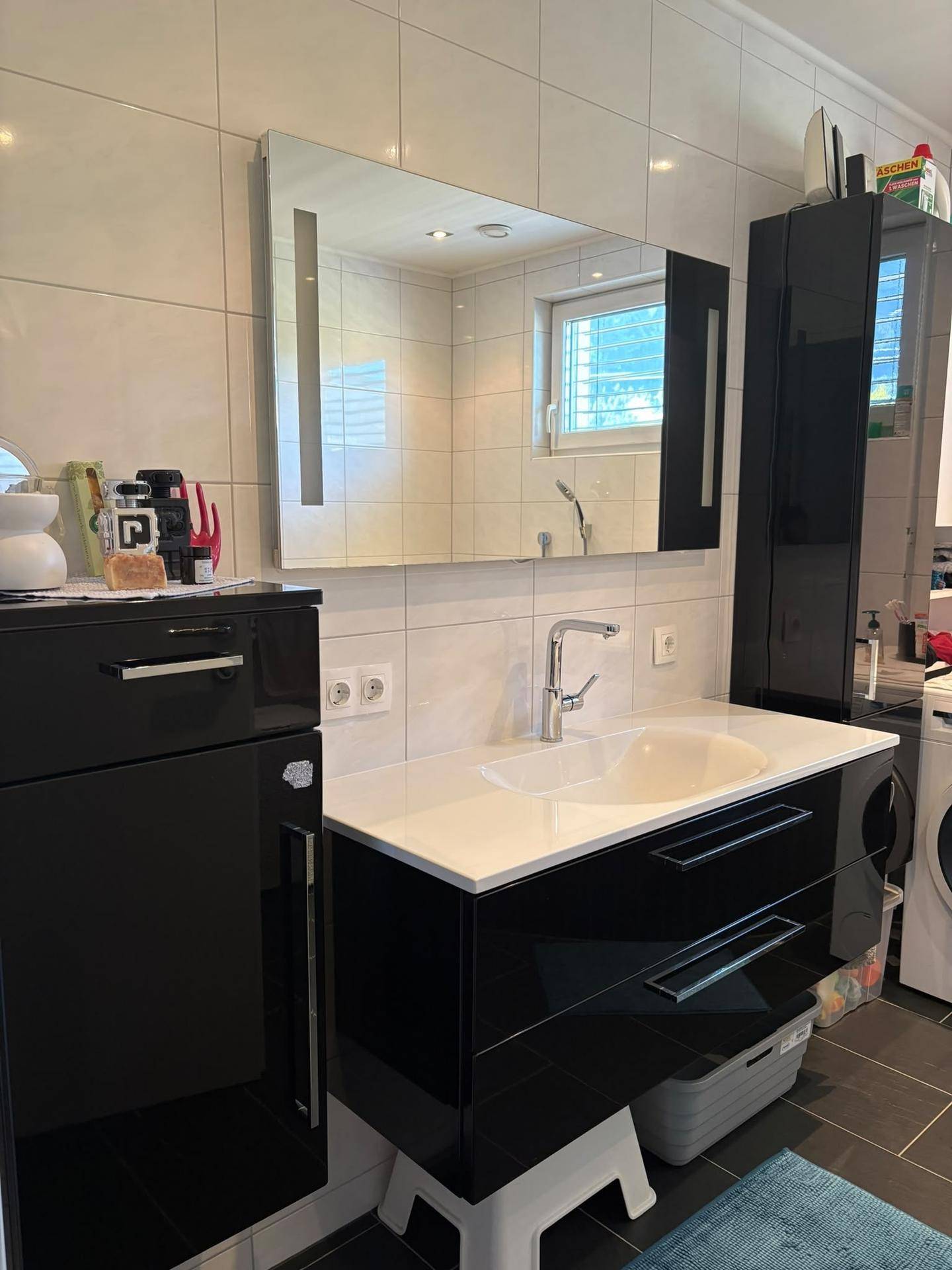 Modernes Badezimmer mit schwarzem Waschtischunterschrank, großem Spiegel und Fenster.