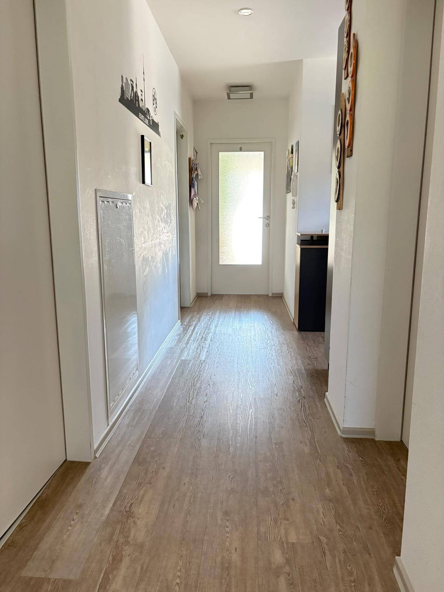 Heller Flur mit Laminatboden und weiß gestrichenen Wänden, der zu weiteren Räumen führt.