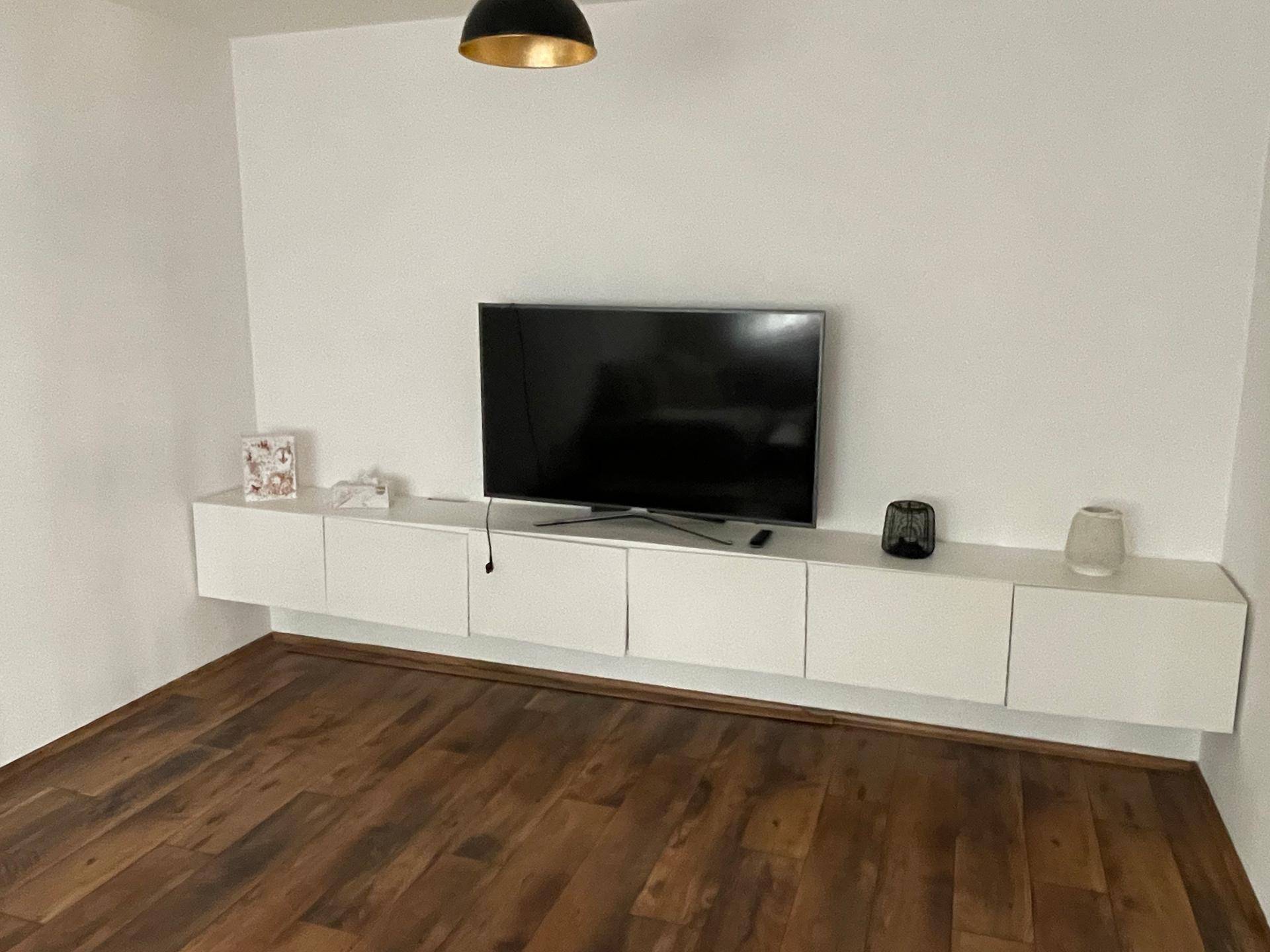Moderner Wohnbereich mit Wandfernseher und schwebenden weißen Schränken.