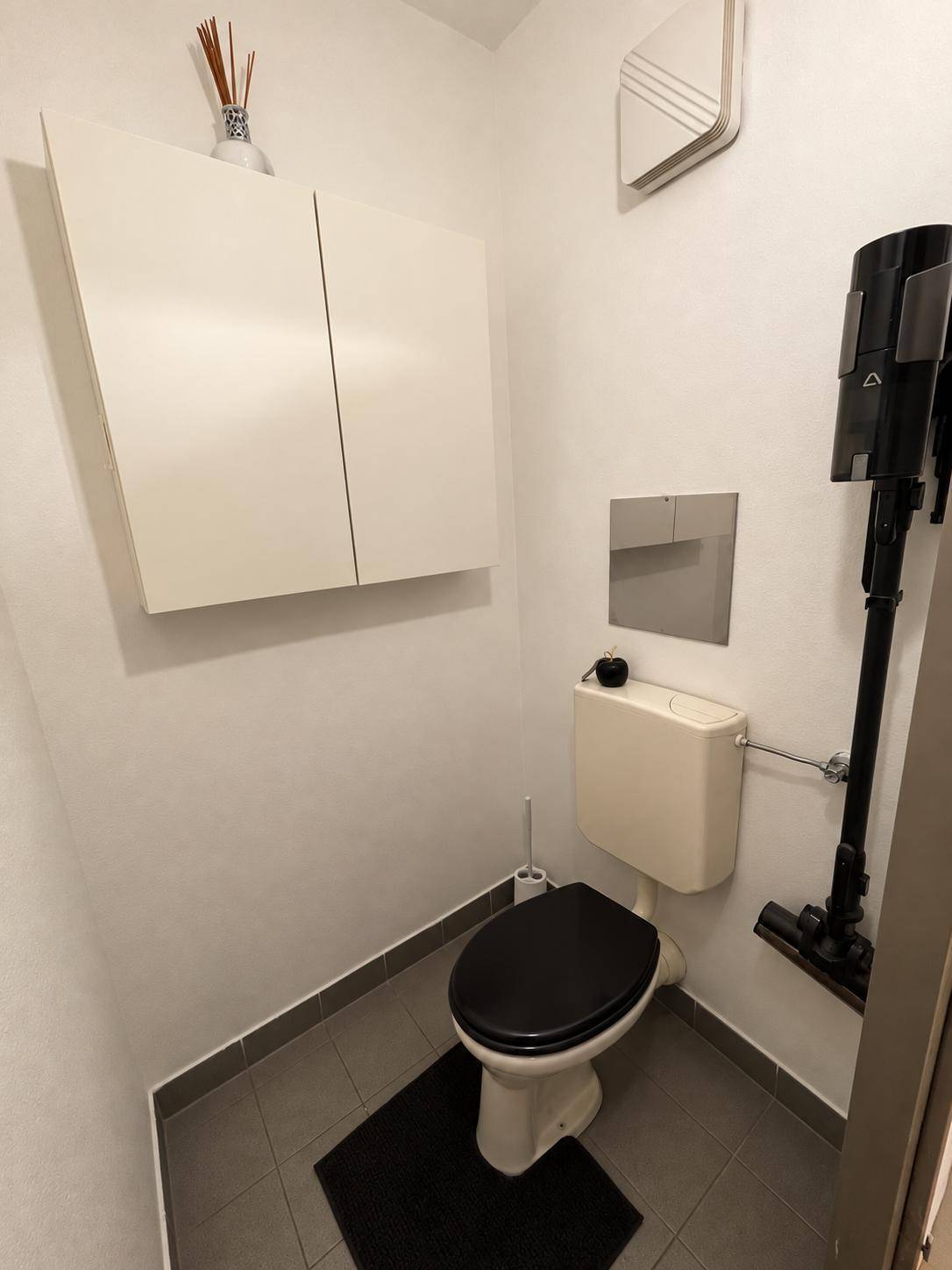 Separates WC mit Toilette, kleinem Waschbecken und Wandregal.