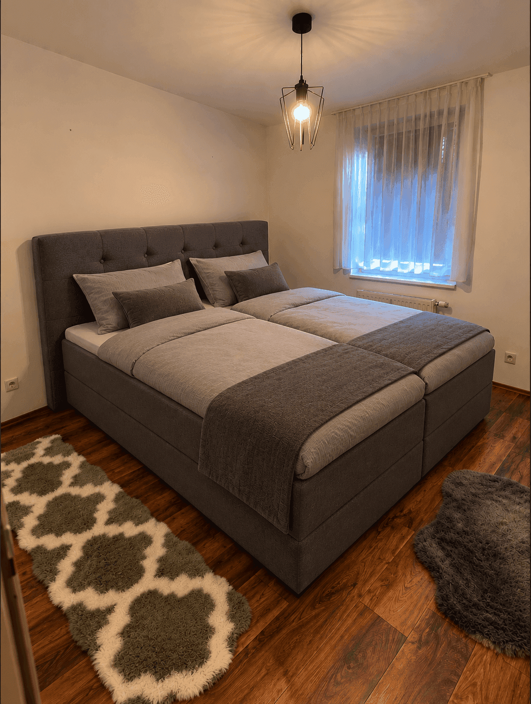 Gemütliches Schlafzimmer mit Doppelbett, Holzboden und Vorhängen am Fenster.