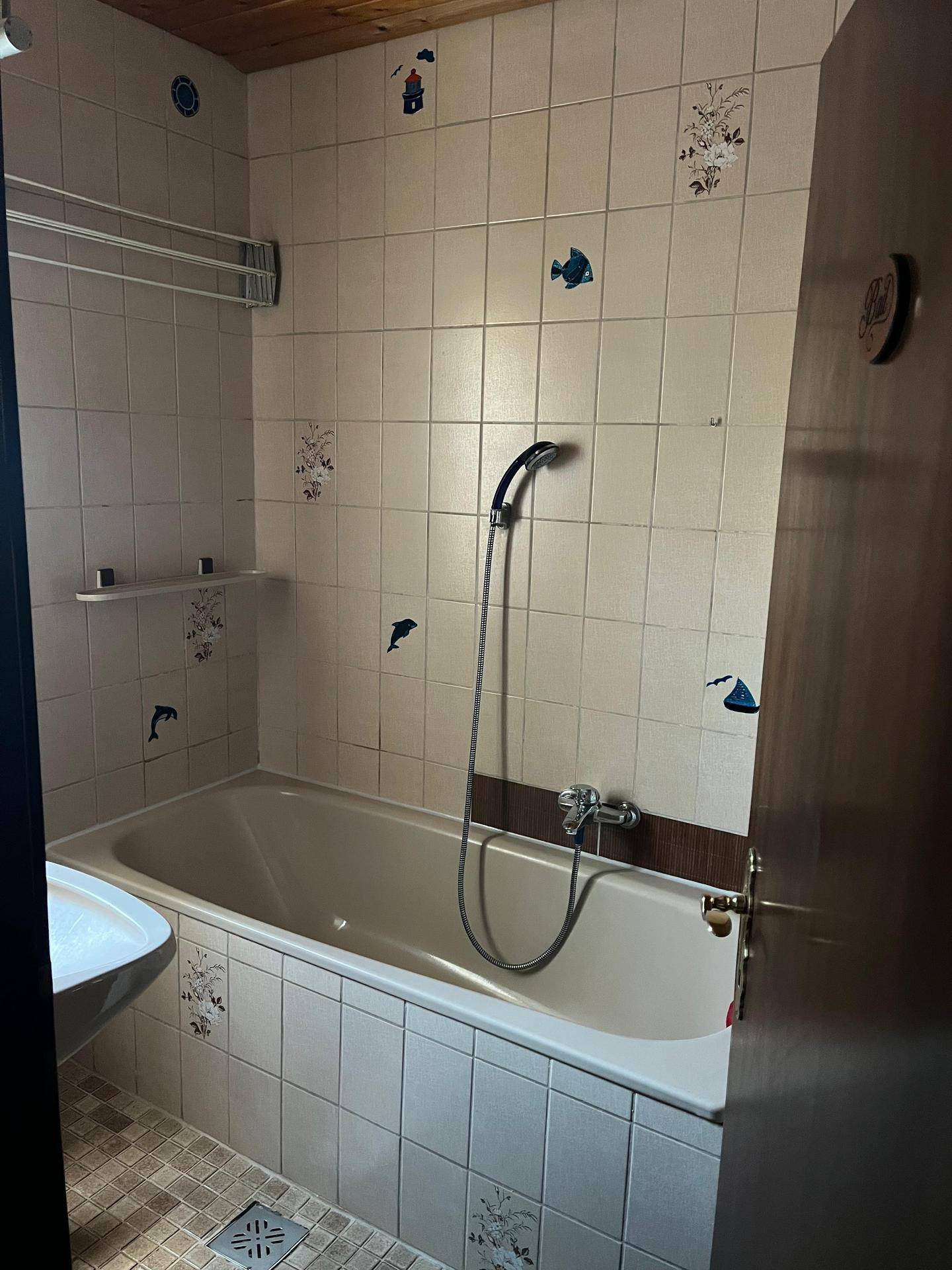 Badezimmer mit Badewanne, Duschfunktion und gefliesten Wänden.