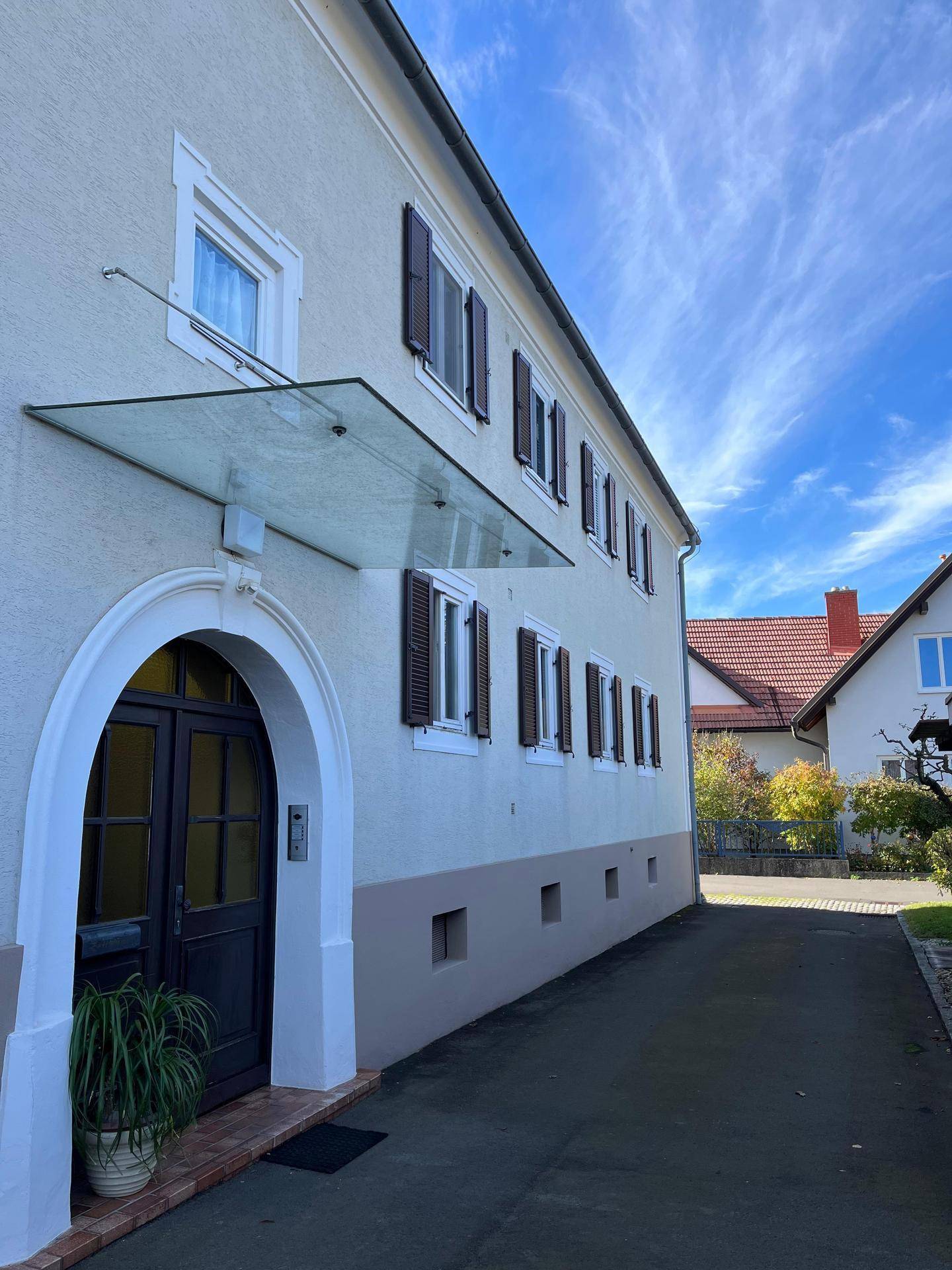 Seitenansicht des Hauses mit braunen Fensterläden und gepflasterter Einfahrt.
