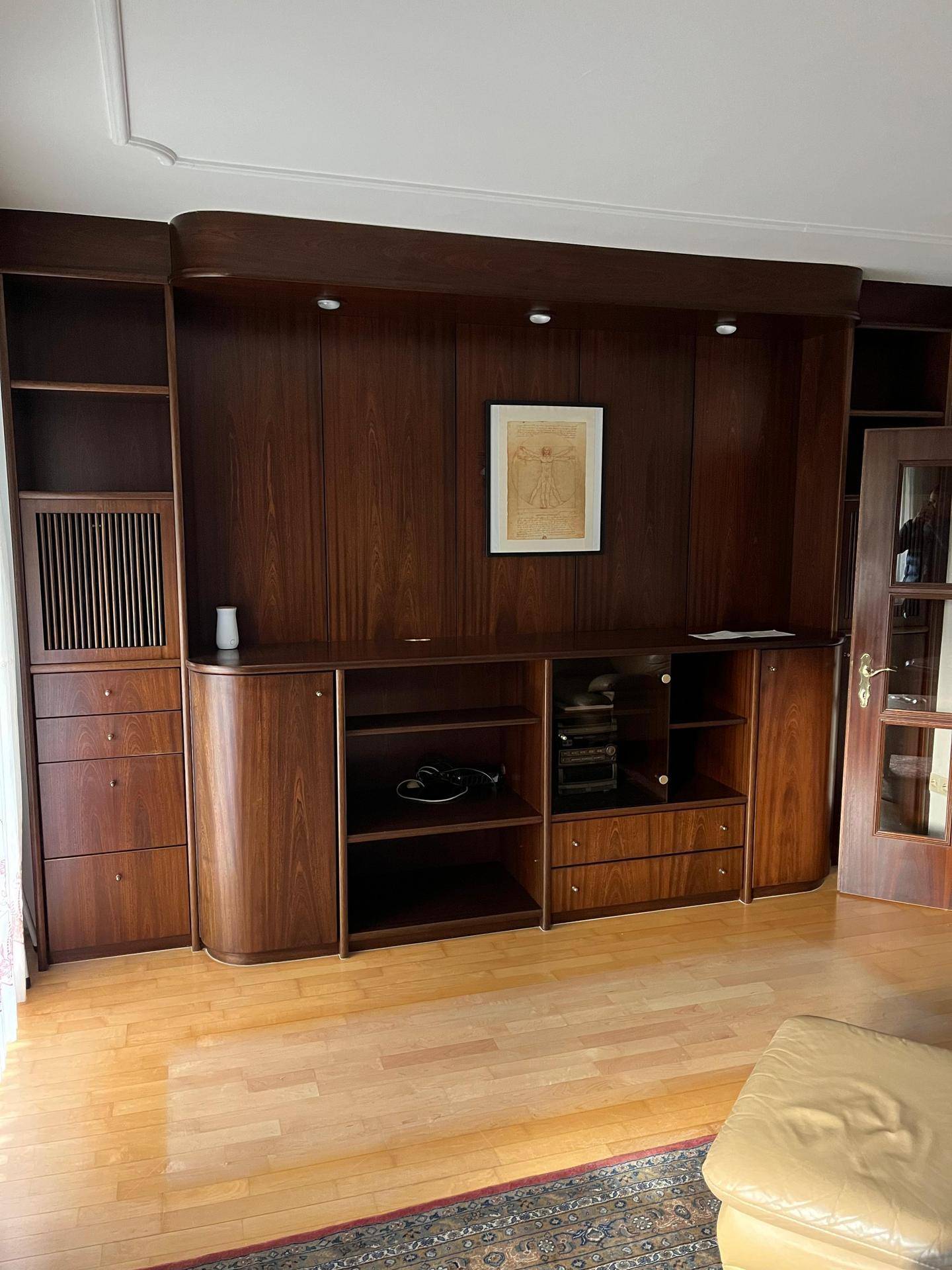 Wohnzimmer mit großer, dunkler Holzschrankwand und Parkettboden.