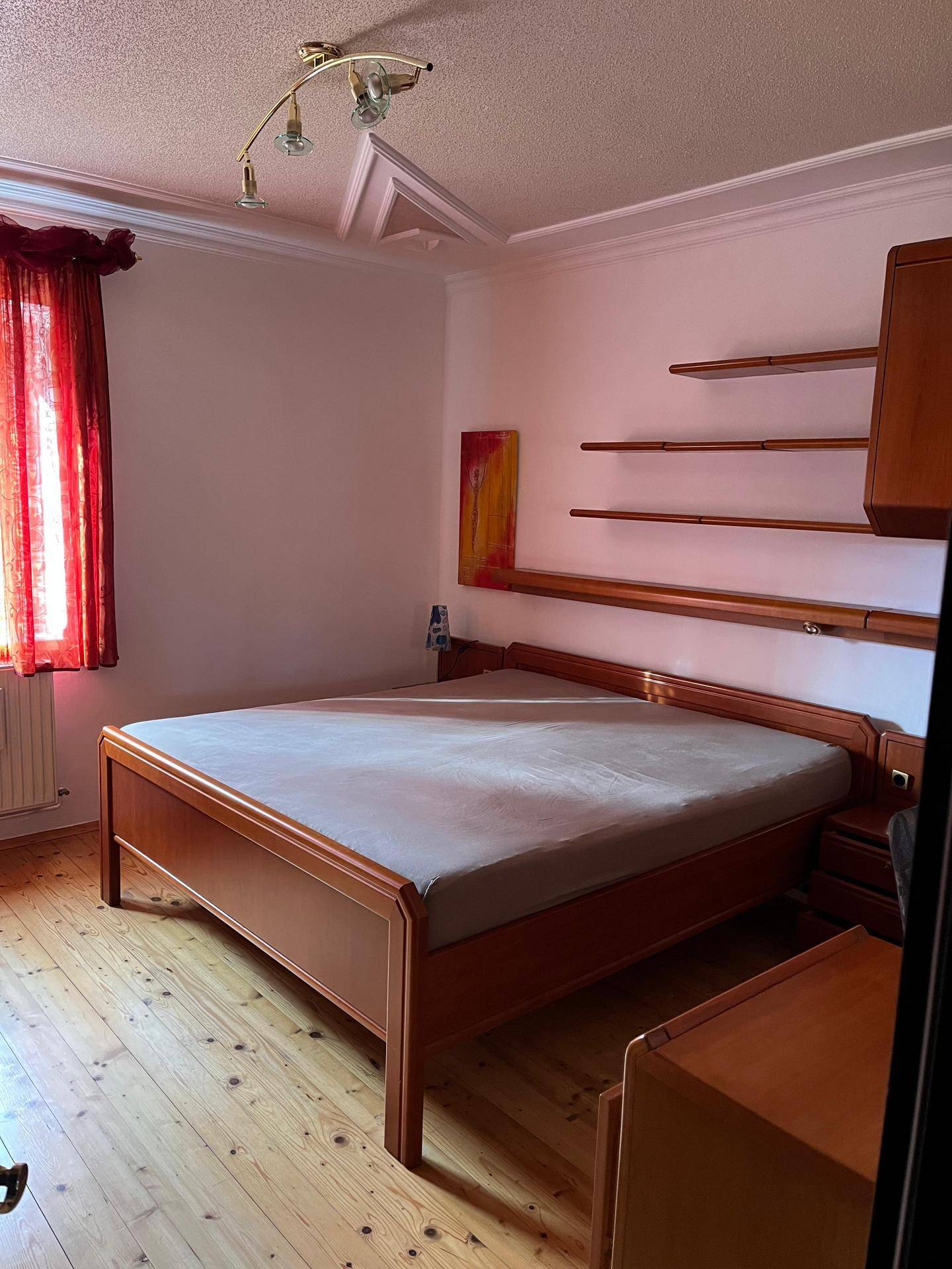 Schlafzimmer mit Holzbett, Parkettboden und rotem Vorhang.