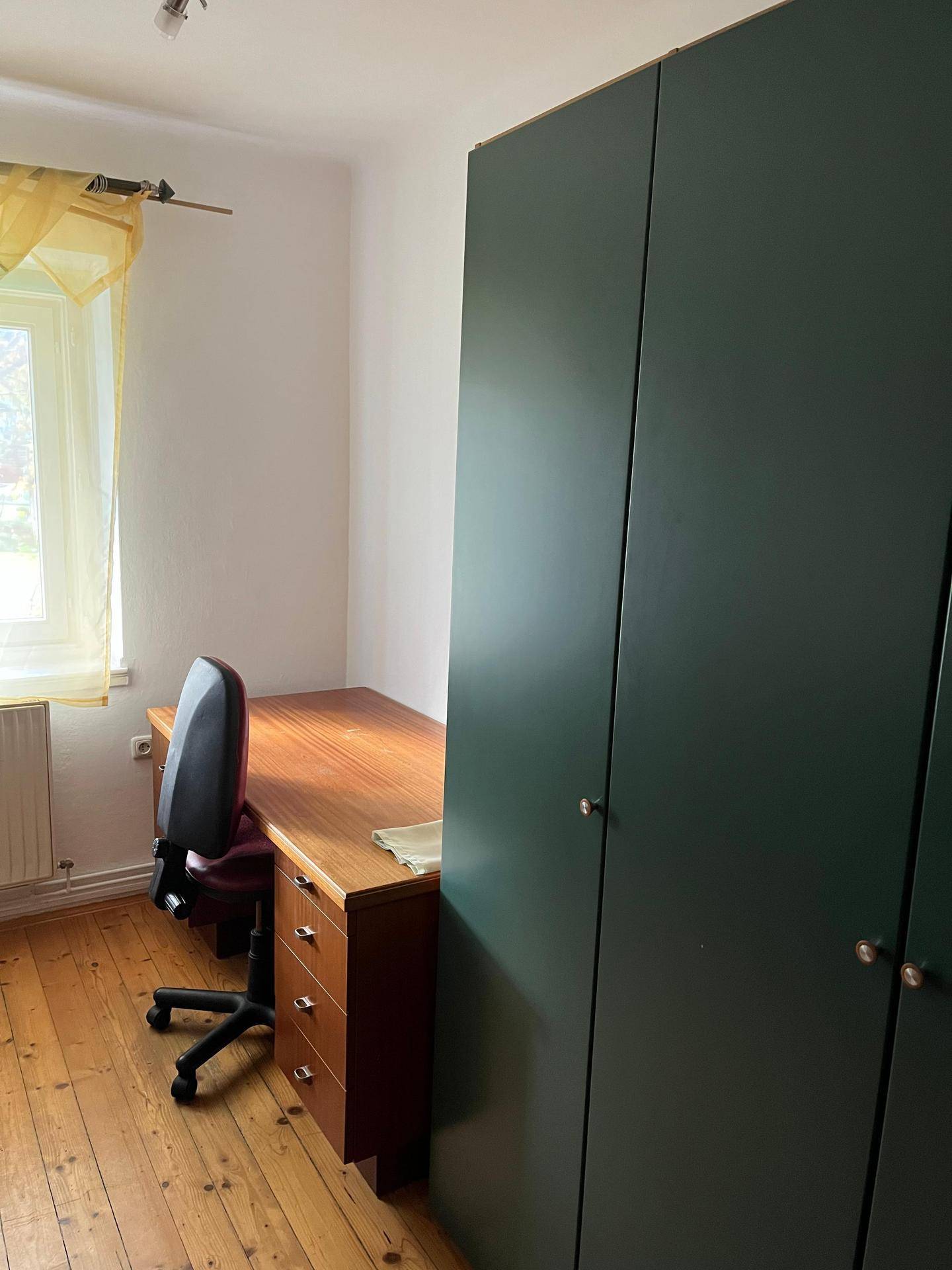 Arbeitszimmer mit Schreibtisch, Bürostuhl und großem Schrank.