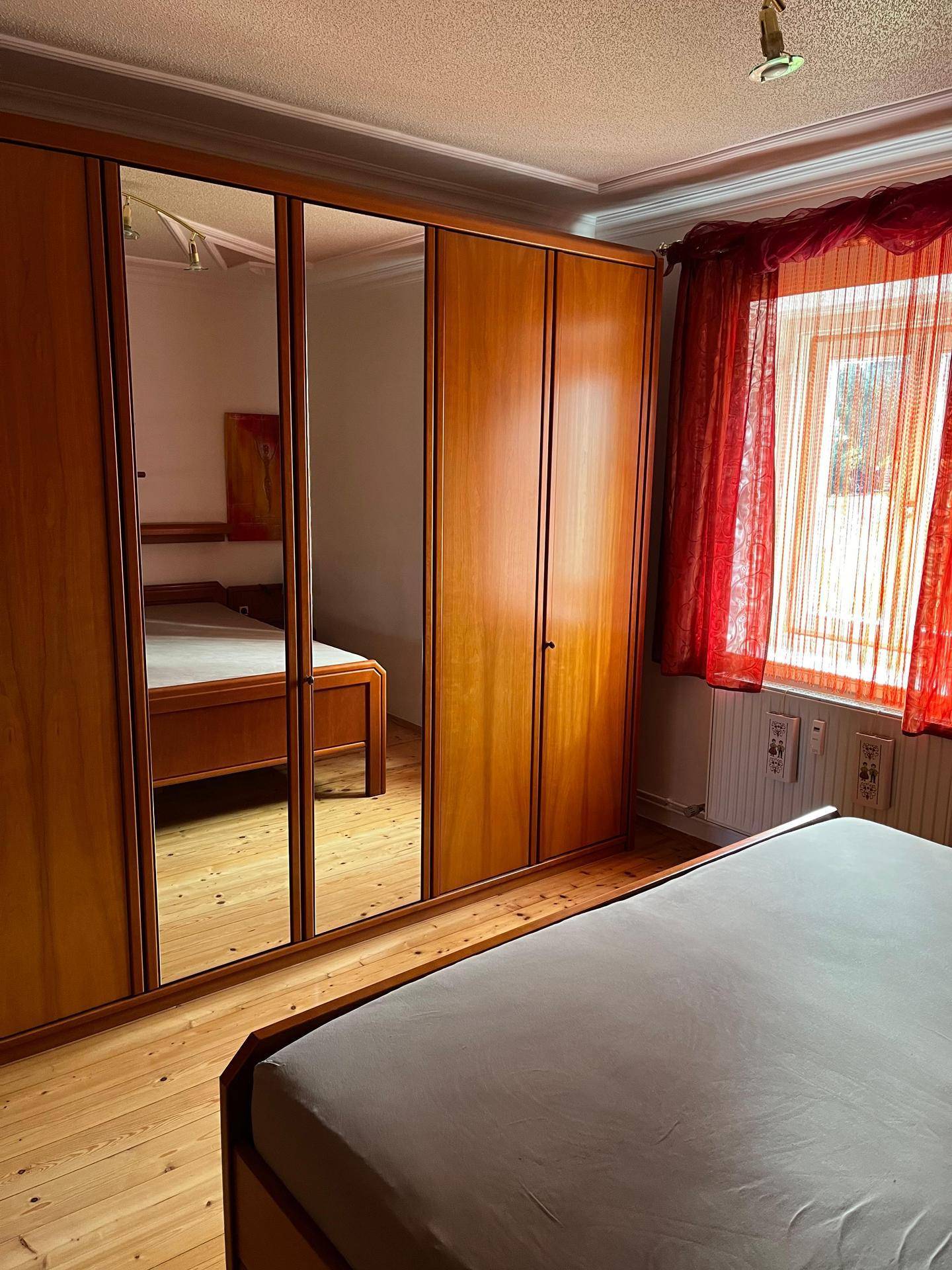 Schlafzimmer mit großem Spiegelschrank, Holzbett und Parkettboden.