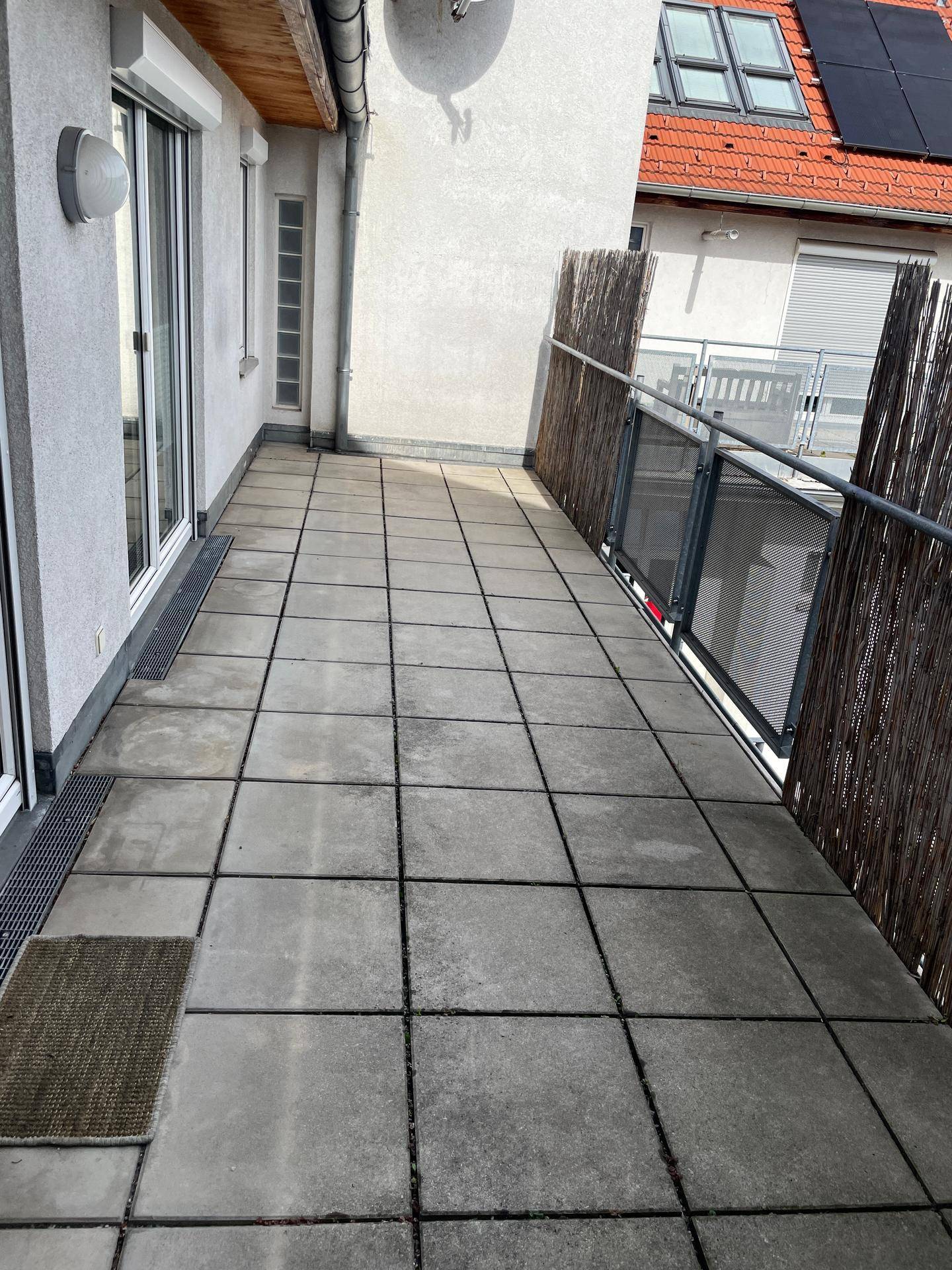 Lange Terrasse mit Fliesenboden und Blick auf die Nachbargebäude.