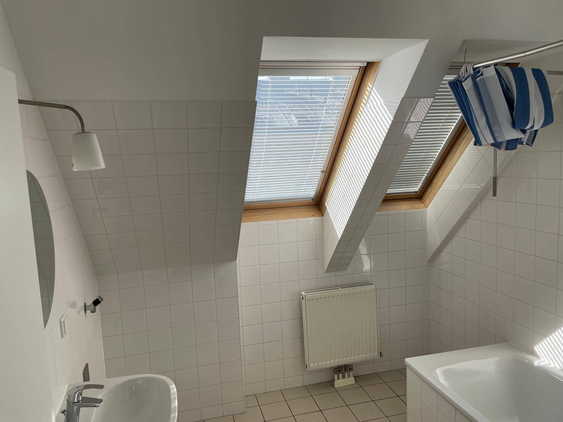Helles Badezimmer mit Badewanne, Fliesen und Dachfenstern.