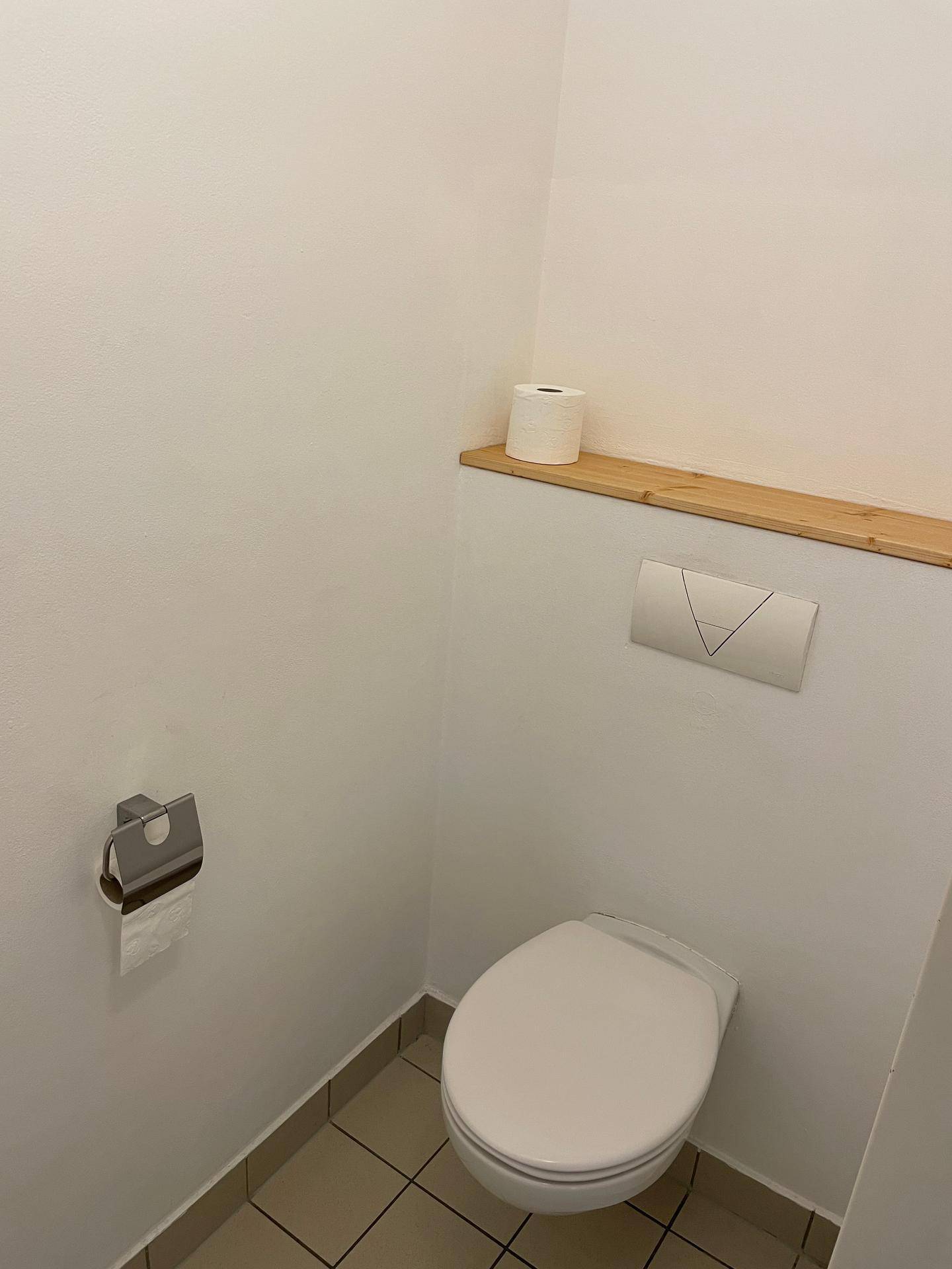 Kleines Gäste-WC mit Wand-WC und einfacher Holzablage.