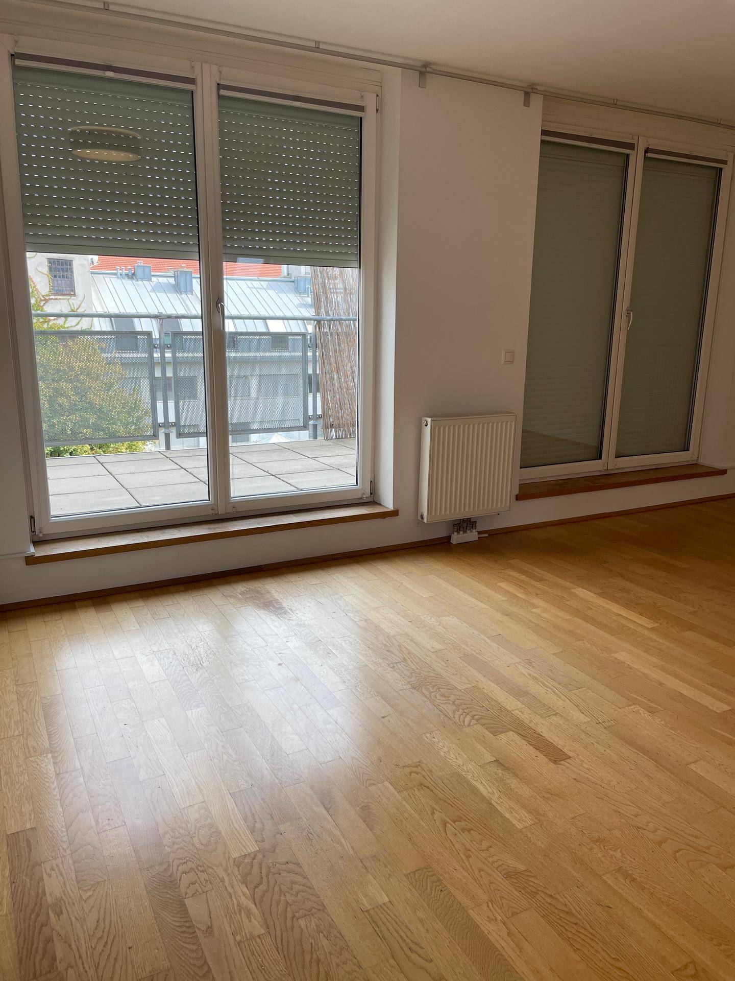 Wohnzimmer mit Parkettboden und großen Fenstern mit Rollläden.