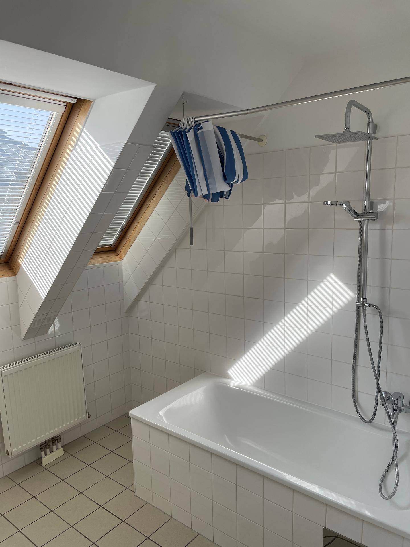 Badezimmer mit Badewanne, Regendusche und Fliesenboden unter Dachfenstern.