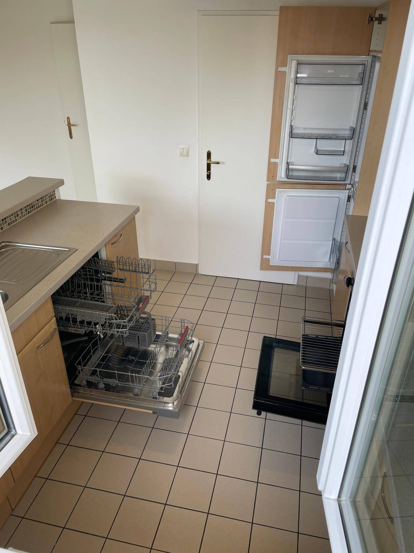 Einbauküche mit Geschirrspüler, Kühlschrank und Fliesenboden.