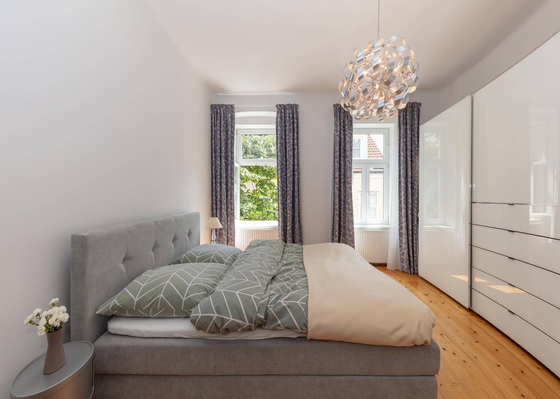 Gemütliches Schlafzimmer mit Doppelbett, Holzboden und großen Fenstern mit Blick ins Grüne.
