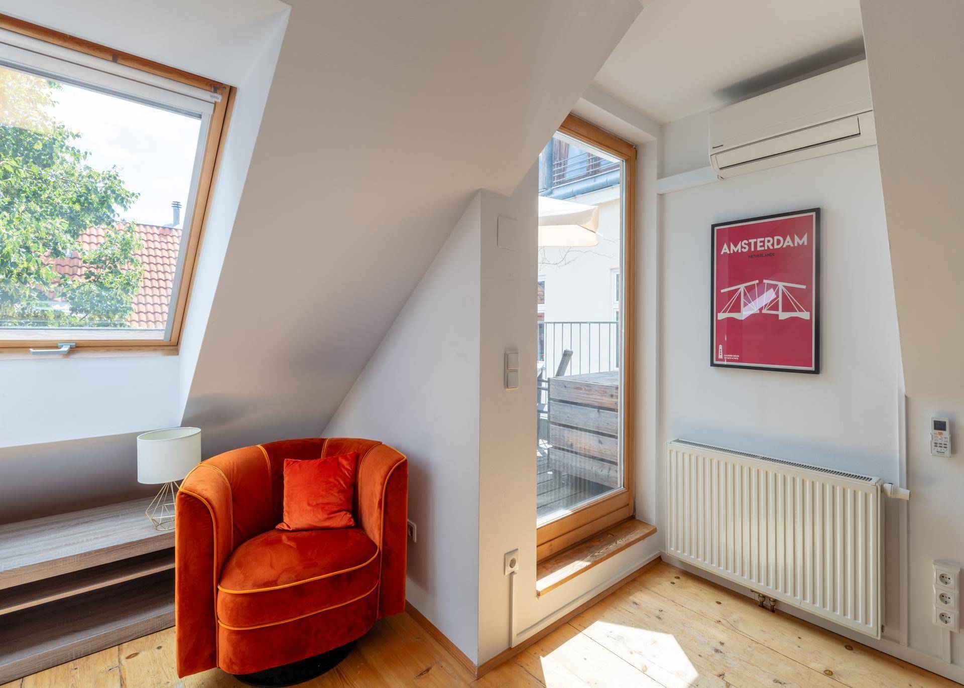Gemütliche Sitzecke mit orangefarbenem Sessel, Holzboden und Zugang zu einem Balkon.
