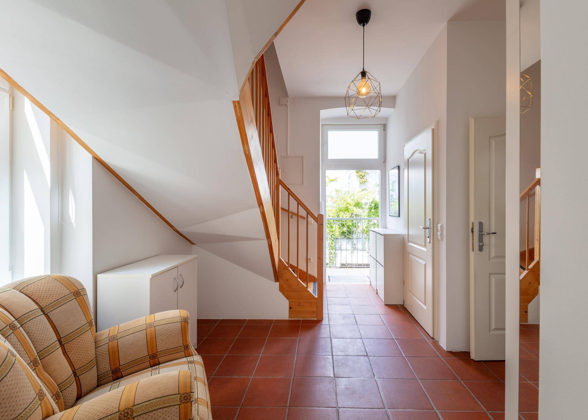 Geräumiger Flur mit Holztreppe, Terrakottafliesen und Zugang zu einem kleinen Balkon.