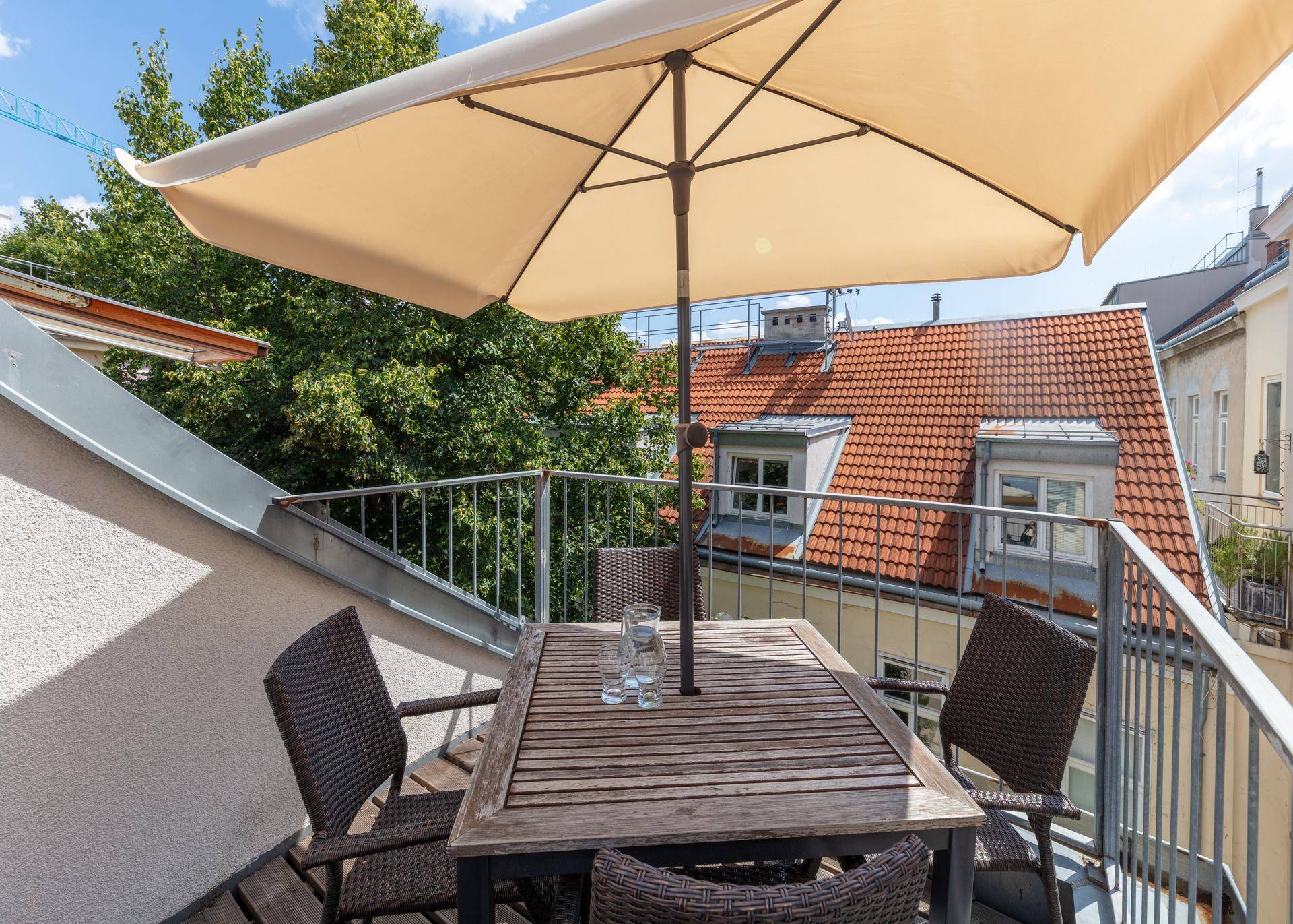 Sonnige Dachterrasse mit Holztisch, Stühlen und Sonnenschirm, umgeben von Dächern.