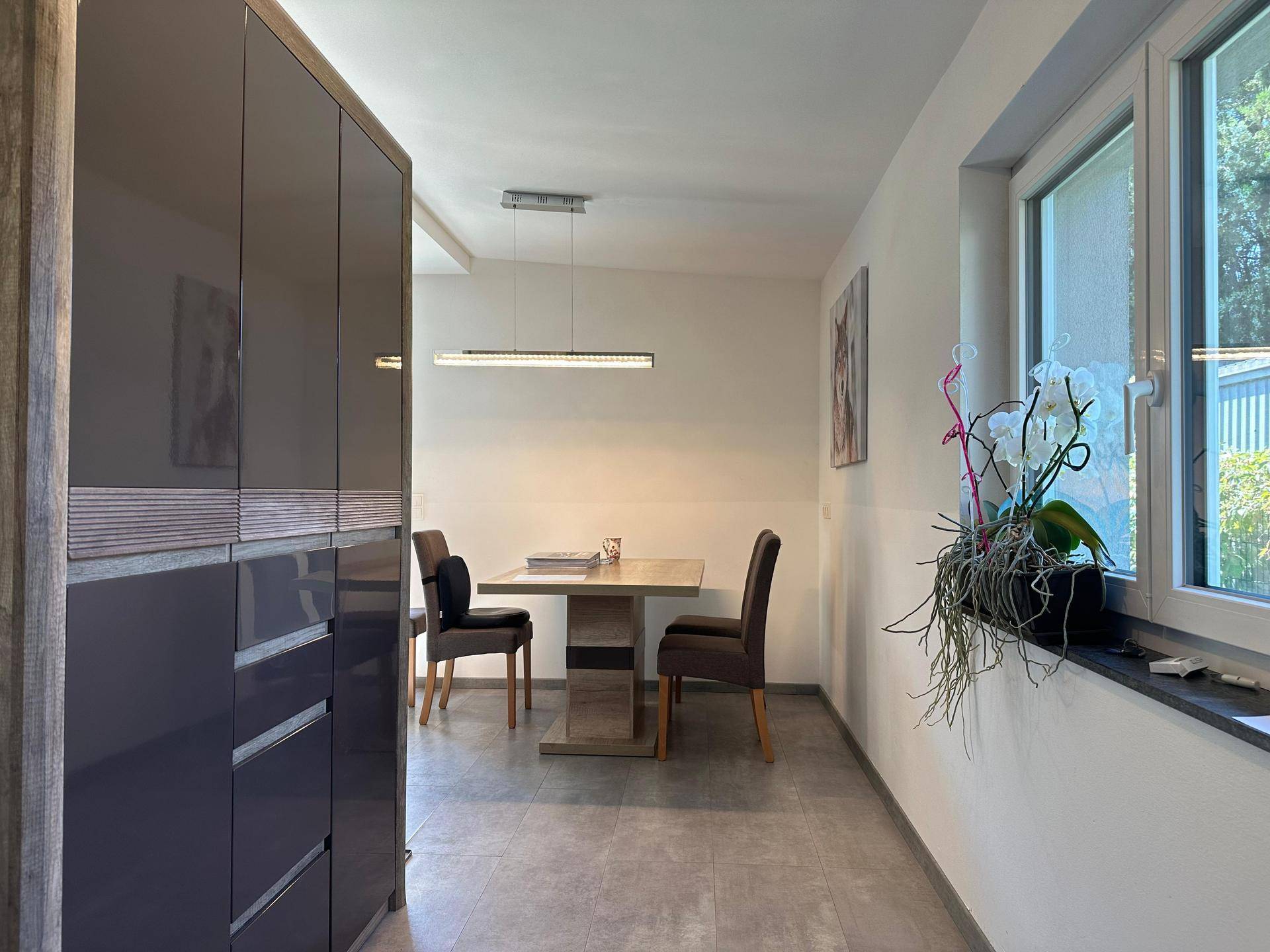 Heller Essbereich mit modernem Sideboard, Fliesenboden und Blick ins Grüne.