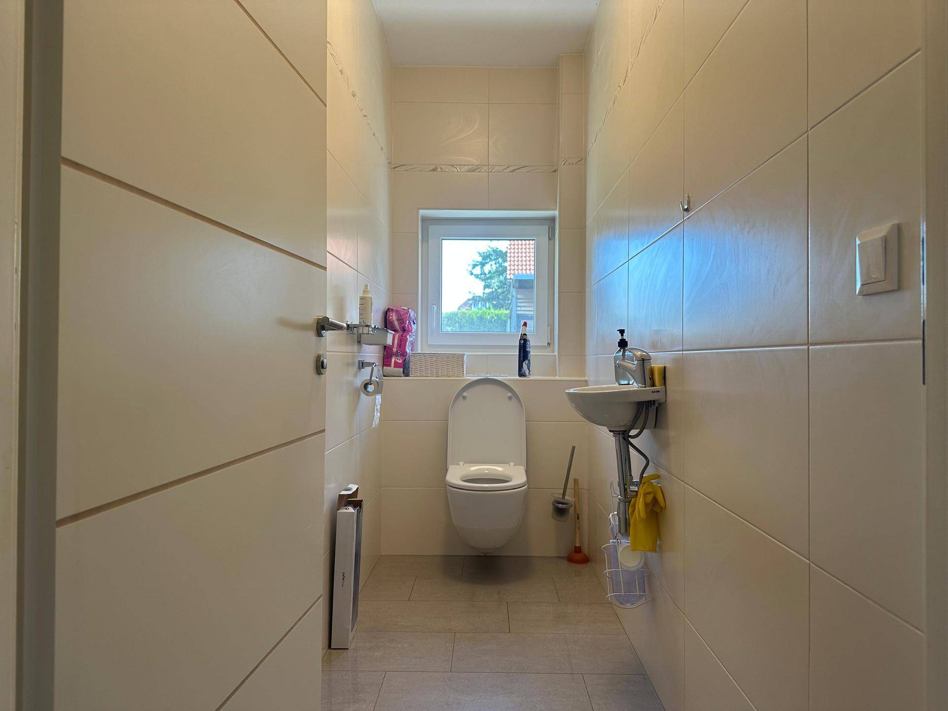 Helles Gäste-WC mit Fenster, wandhängendem WC und kleinem Handwaschbecken.
