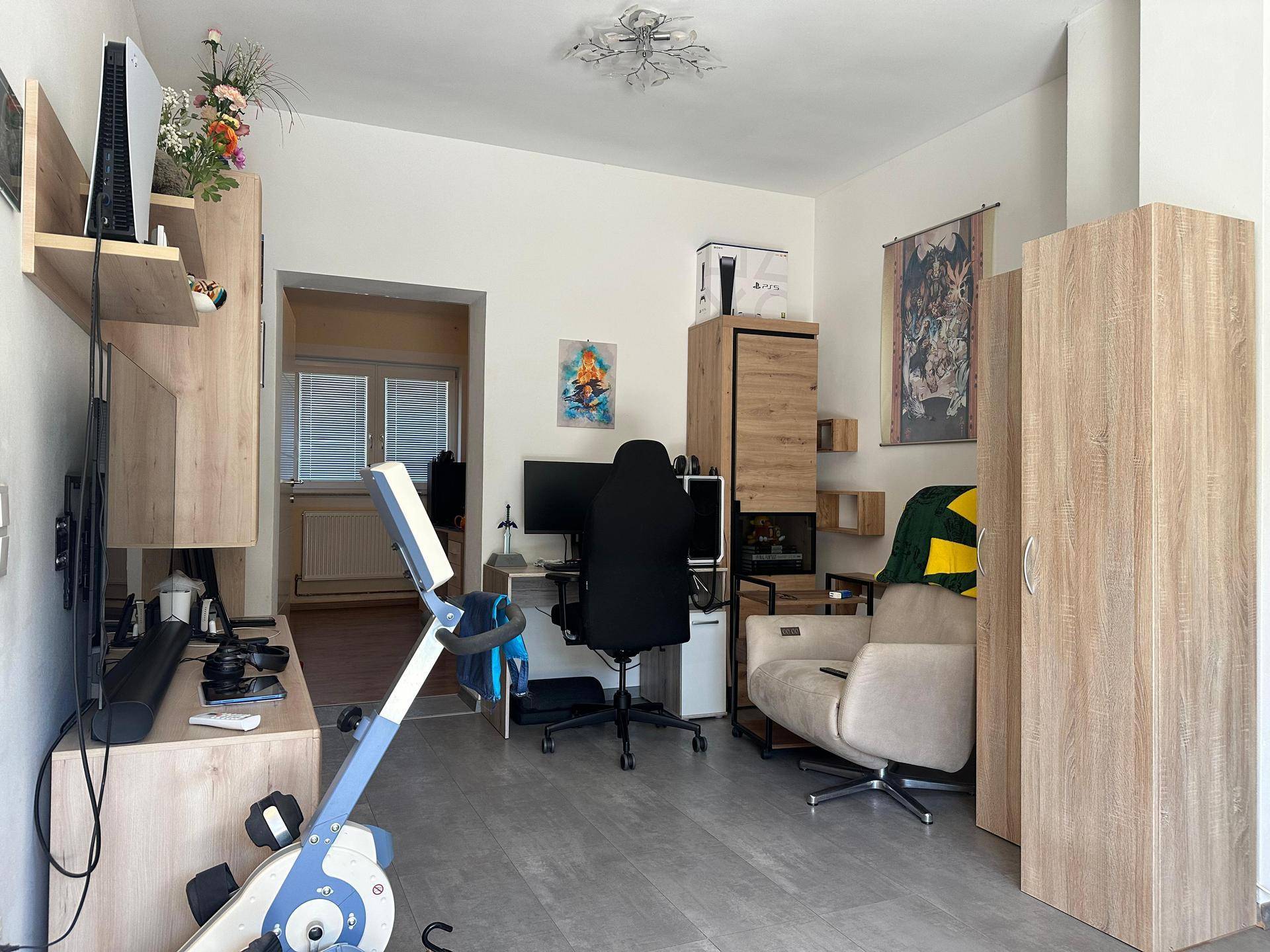 Vielseitiger Wohnraum mit Arbeitsbereich, Fitnessgerät und modernen Holzmöbeln.