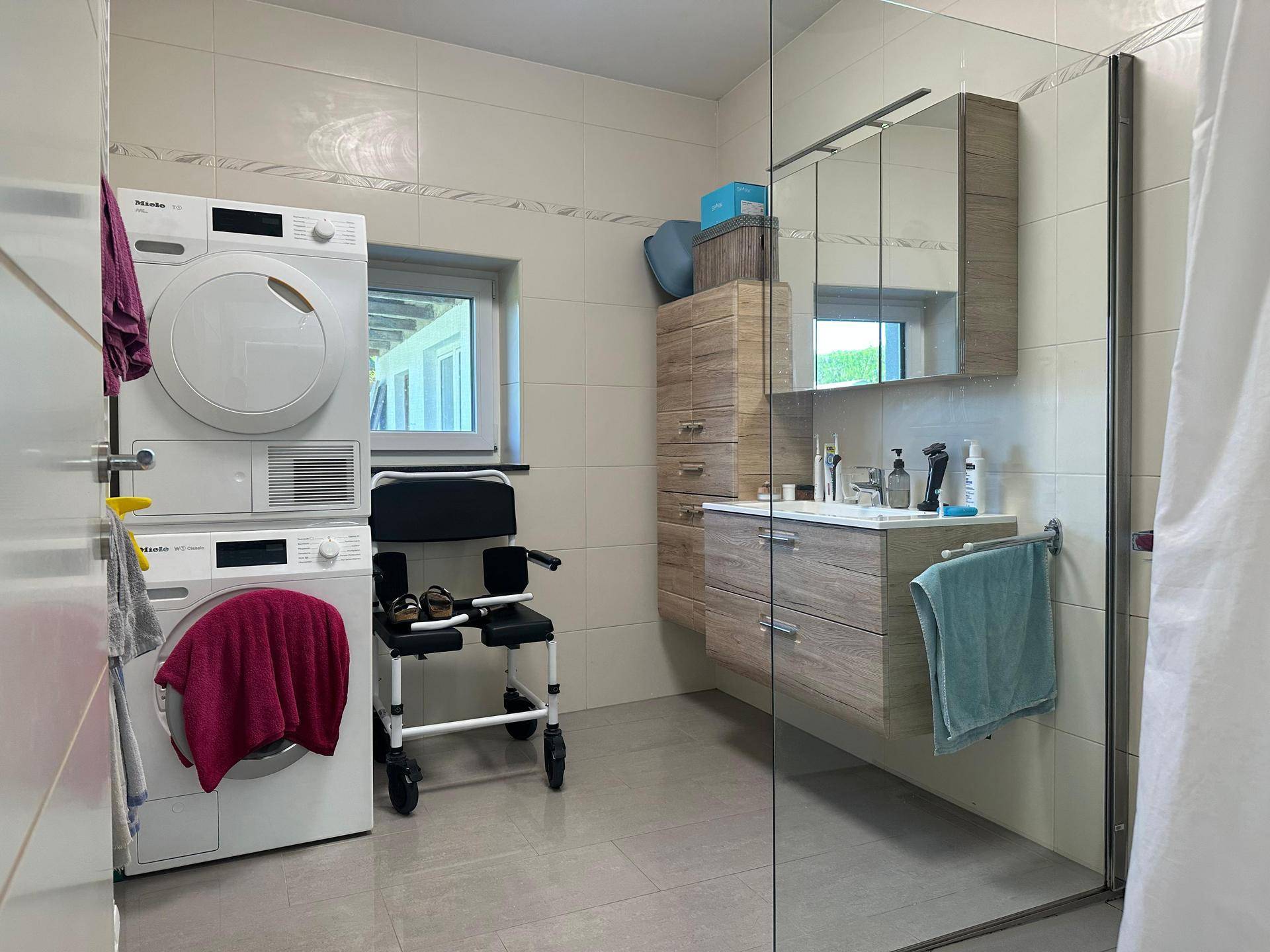 Modernes Badezimmer mit ebenerdiger Dusche, Waschmaschine, Trockner und barrierefreiem Zugang.