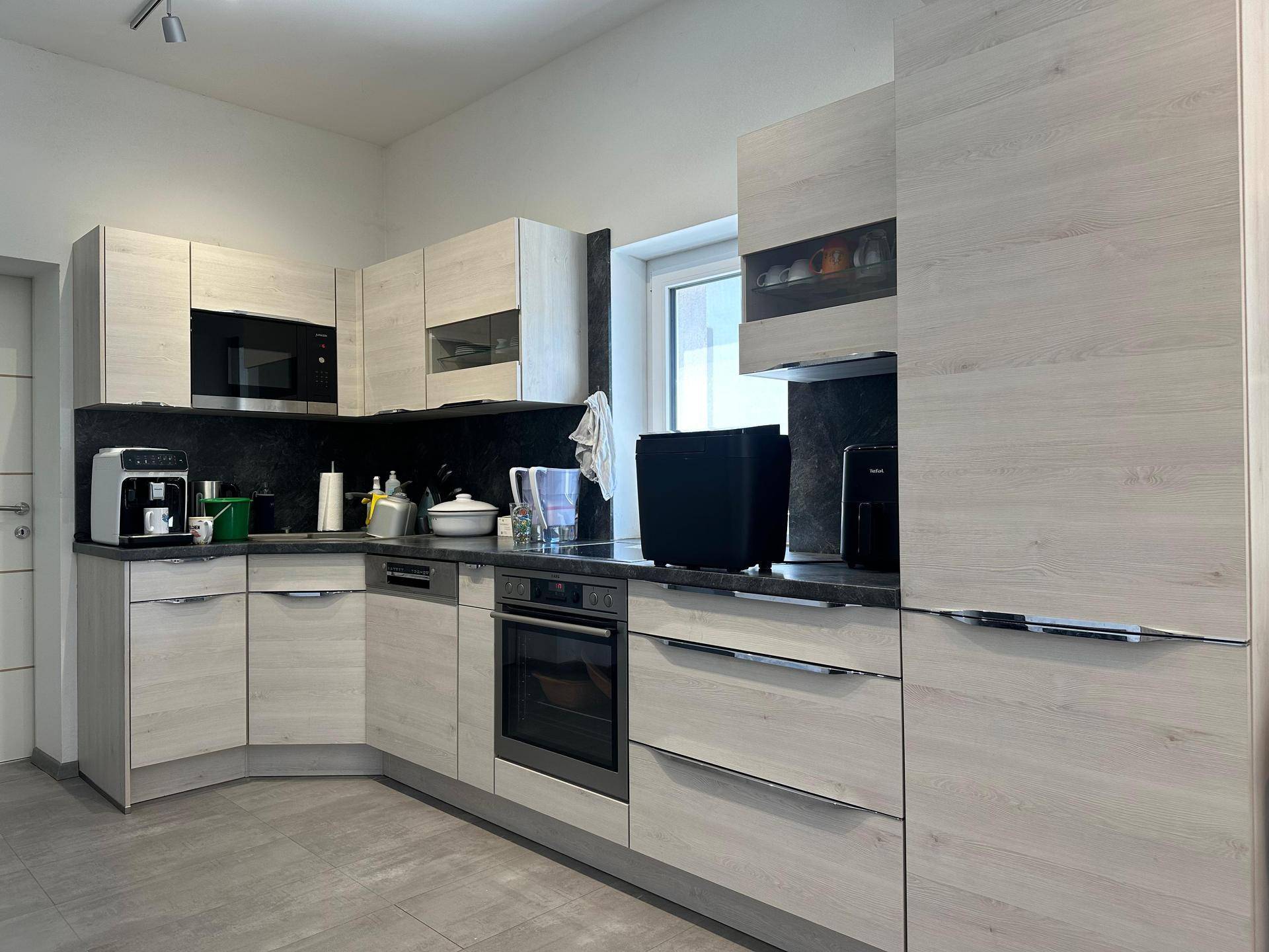 Moderne Einbauküche mit hellen Holzfronten, dunkler Arbeitsplatte und integrierten Geräten.