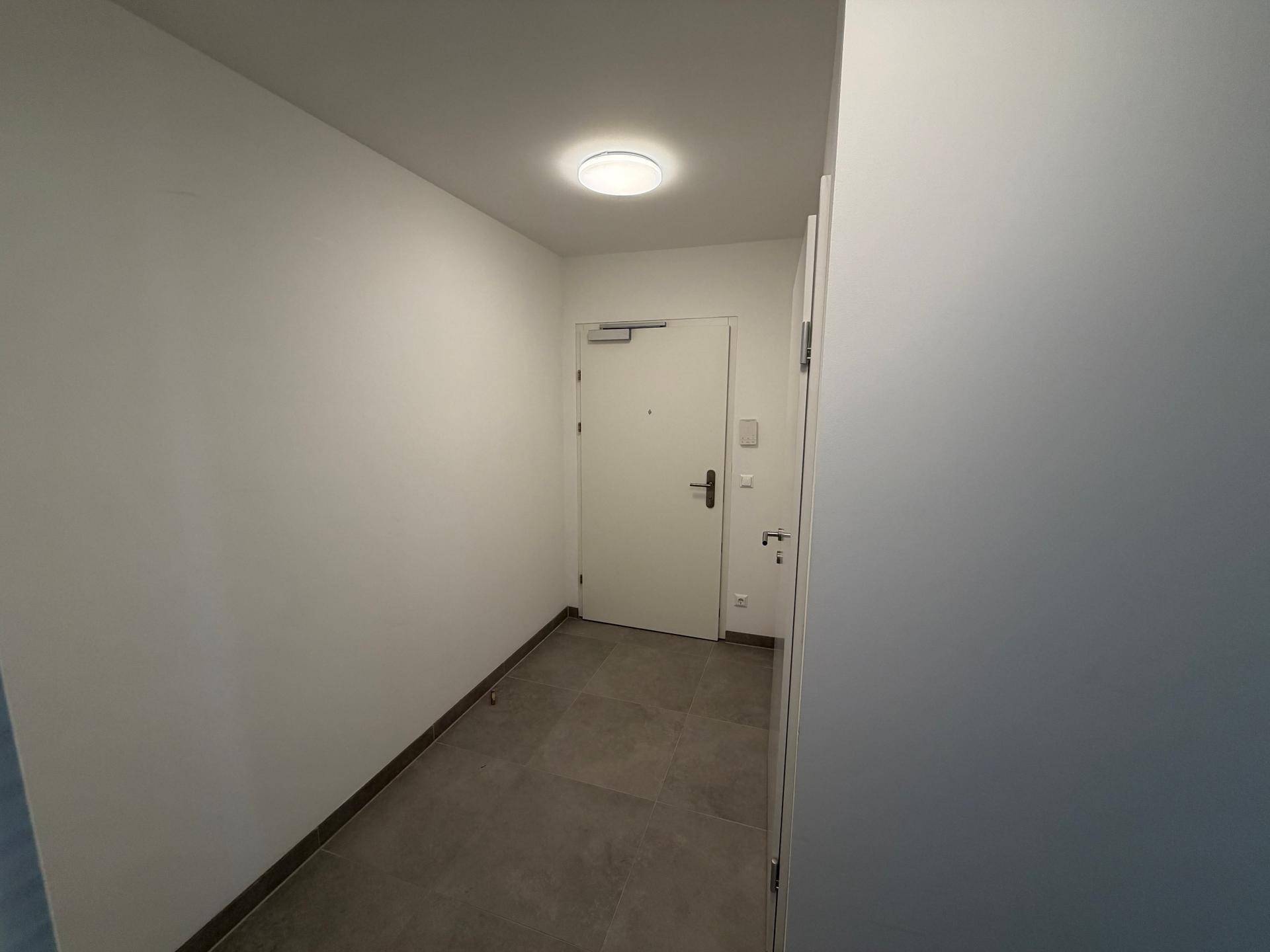 Heller Eingangsbereich mit Fliesenboden, weißer Eingangstür und schlichten Wänden.