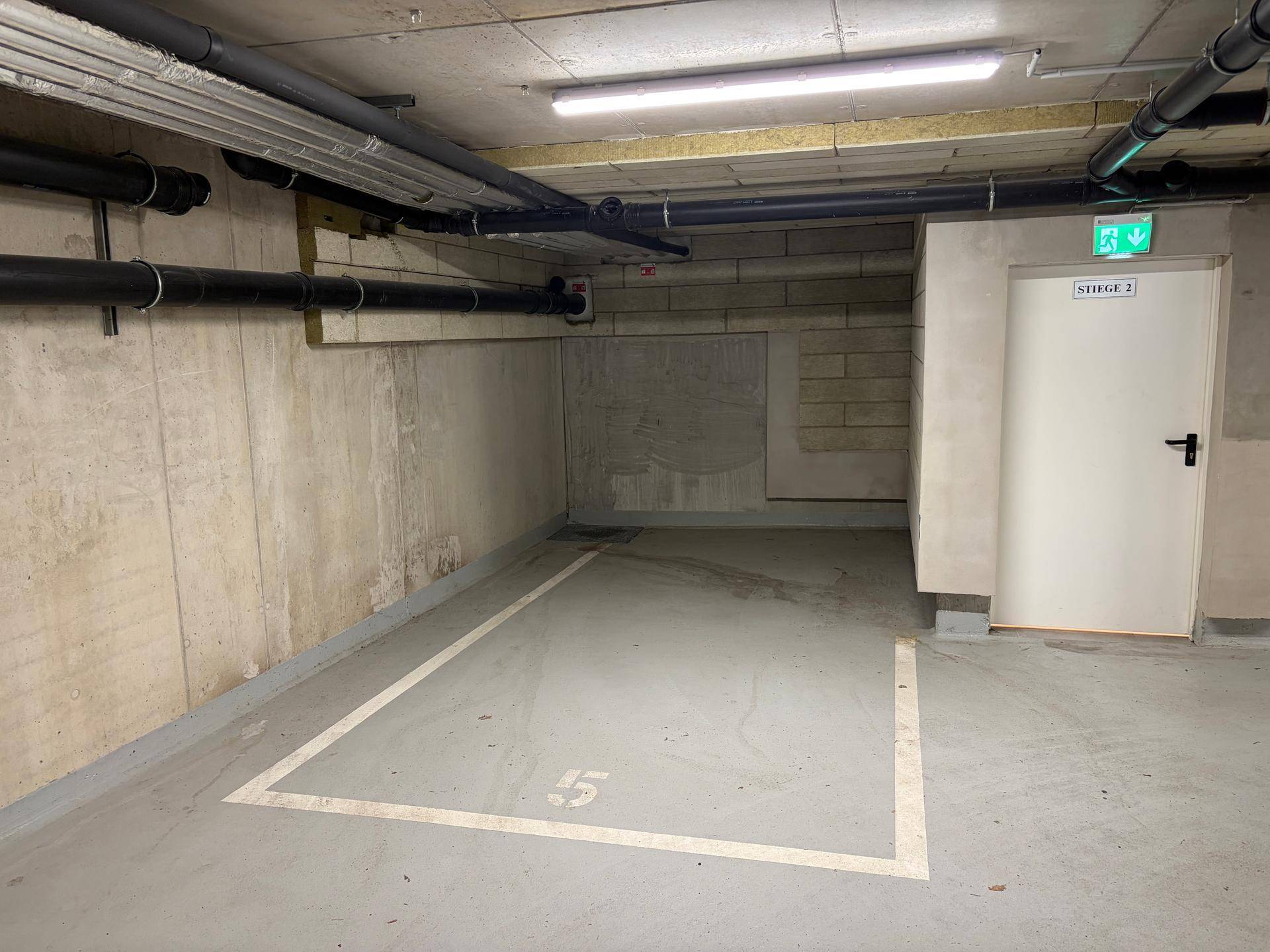 Tiefgaragenstellplatz in einem modernen Gebäude mit Betonwänden und sichtbaren Rohren.