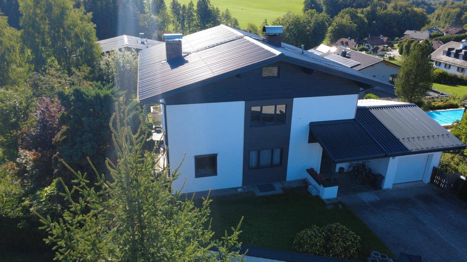 Ansicht des Hauses von der Seite mit Garten, Garage, Photovoltaikanlage und umliegender Natur.
