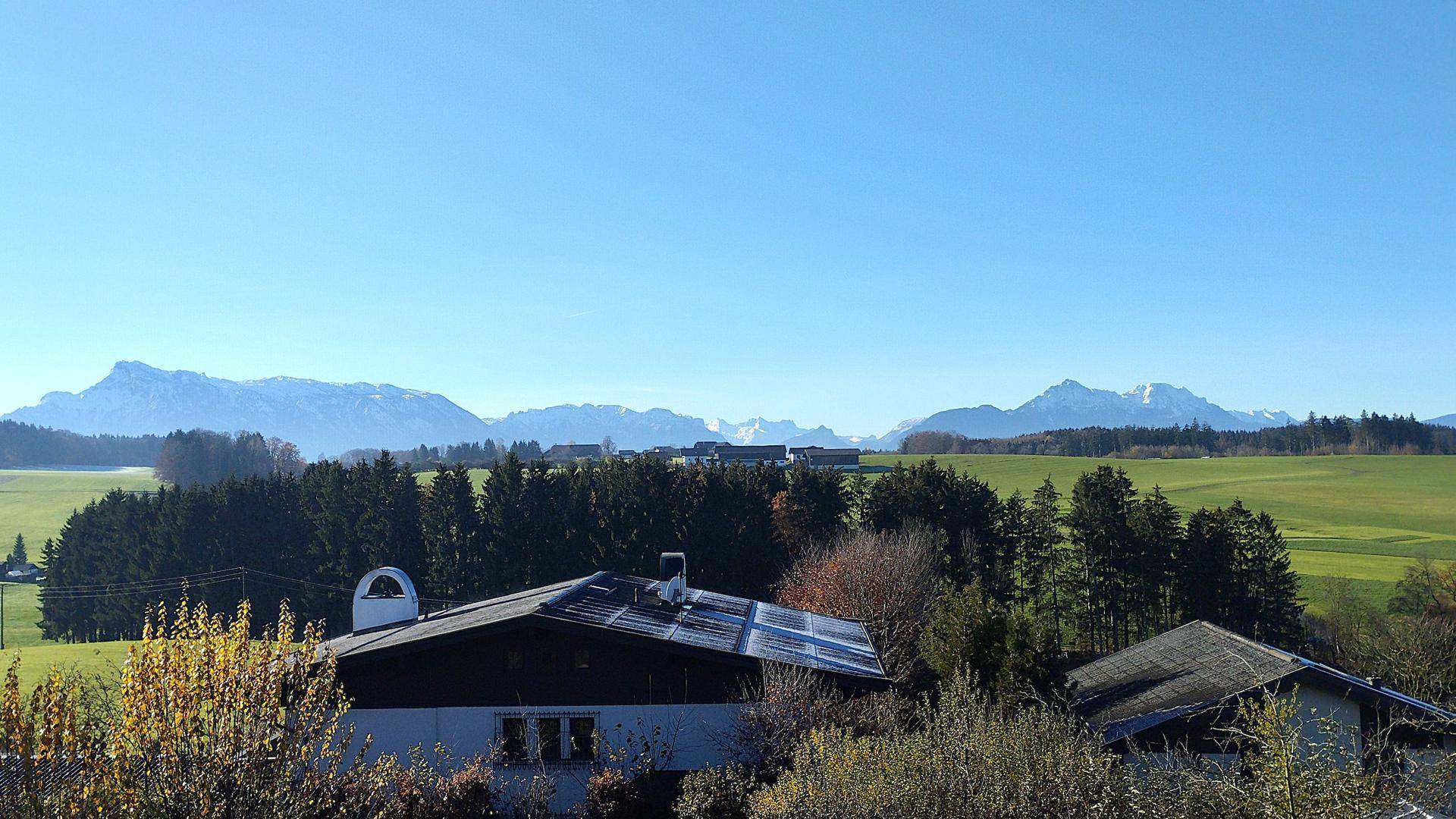 Weitläufiger Blick auf die umliegende Landschaft mit grünen Feldern und schneebedeckten Bergen im Hintergrund.