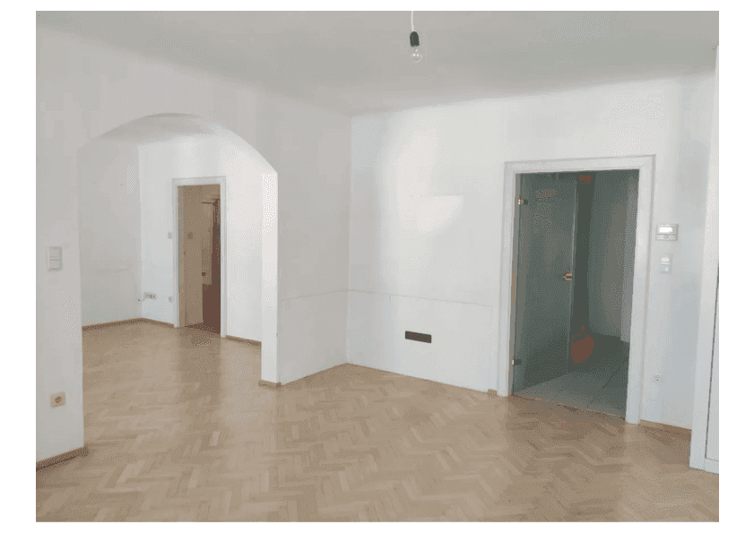 Geräumiger Wohnbereich mit Parkettboden, weiß gestrichenen Wänden und Glastür.