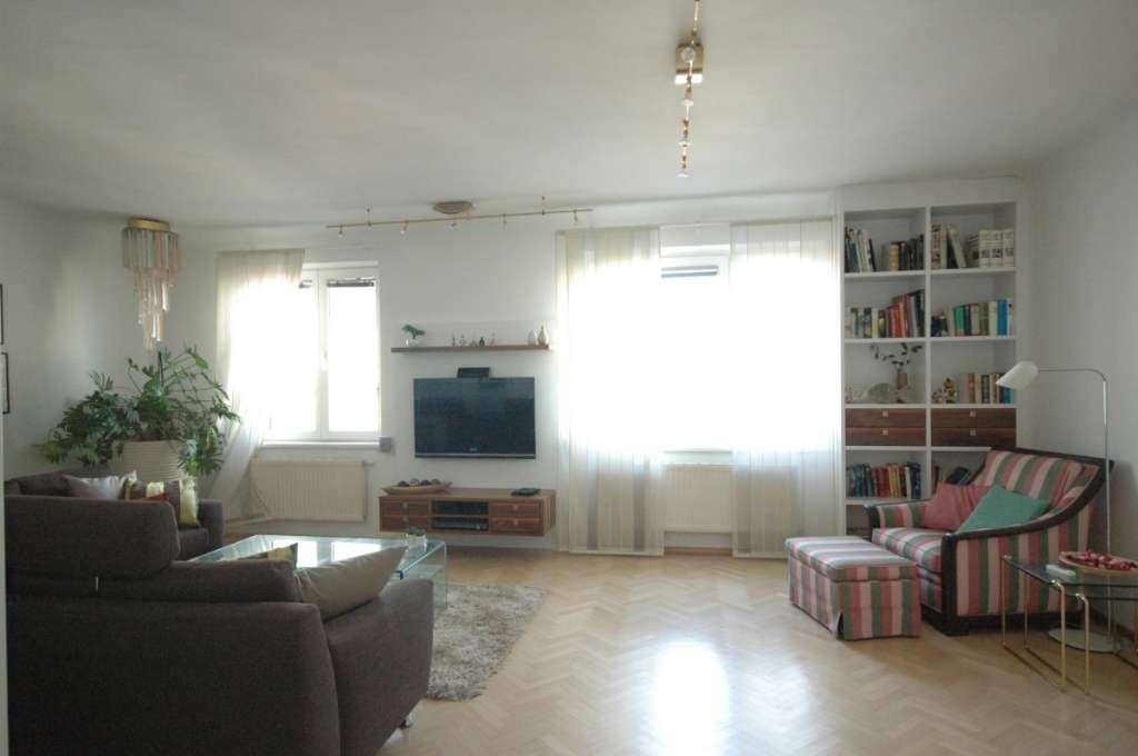 Geräumiges Wohnzimmer mit Parkettboden, Bücherregal und viel Tageslicht.