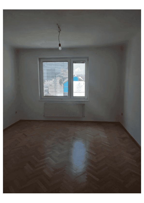 Leeres Zimmer mit Parkettboden, Fenster und Heizkörper, bereit zur individuellen Gestaltung.