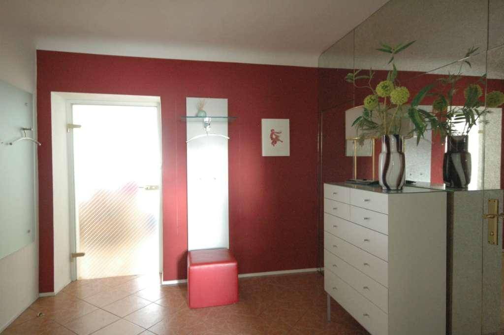 Eingangsbereich mit roter Akzentwand, Spiegeln und praktischer Kommode.