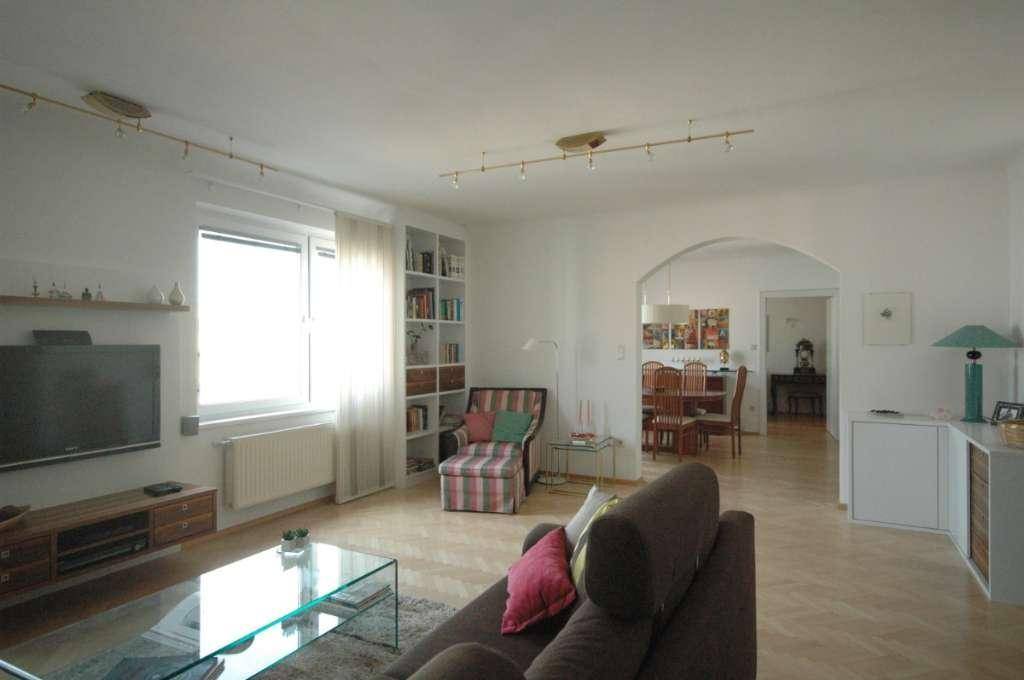 Offener Wohn- und Essbereich mit Parkettboden, Sofa und Bücherregal.