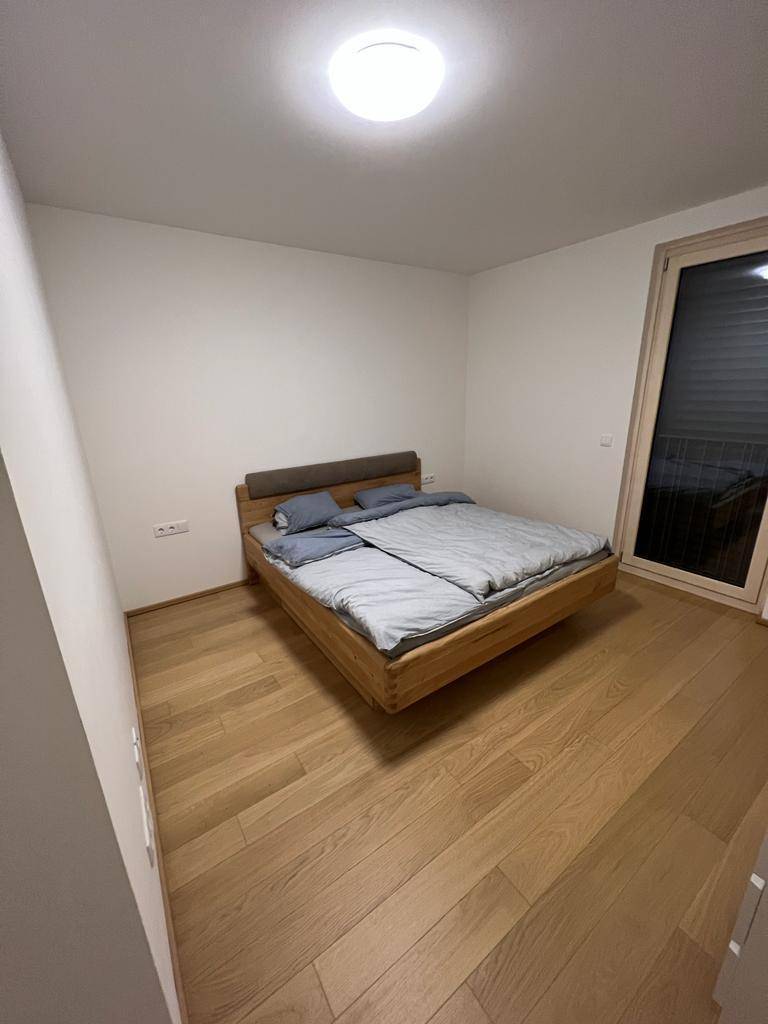 Schlafzimmer mit Holzbett, Holzboden und großem Fenster für natürliches Licht.