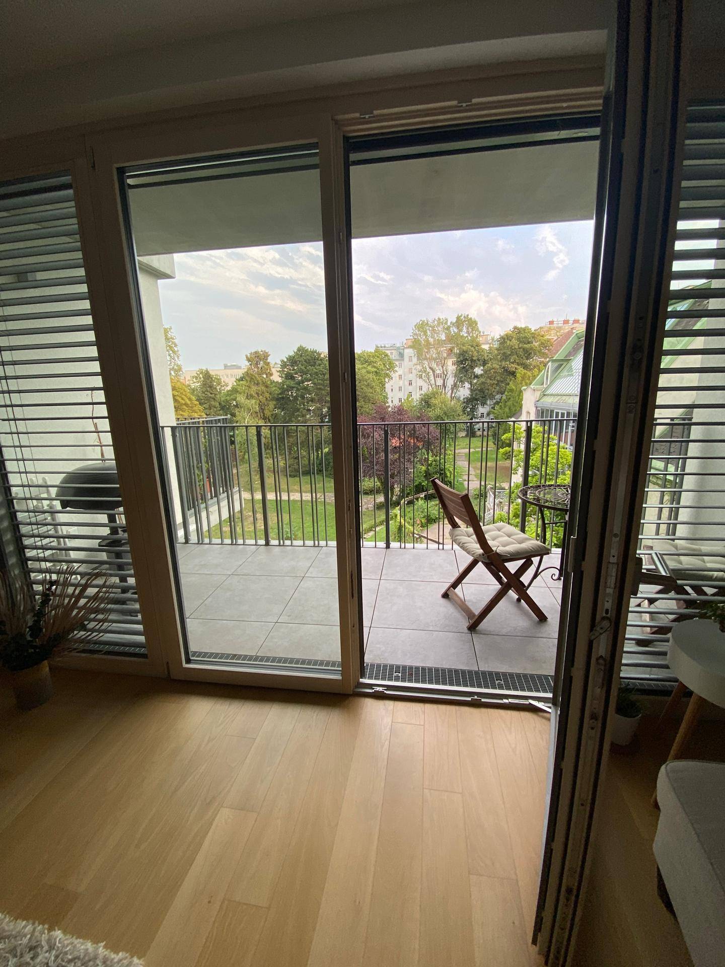Balkon mit Fliesenboden, Sitzgelegenheit und Blick ins Grüne.