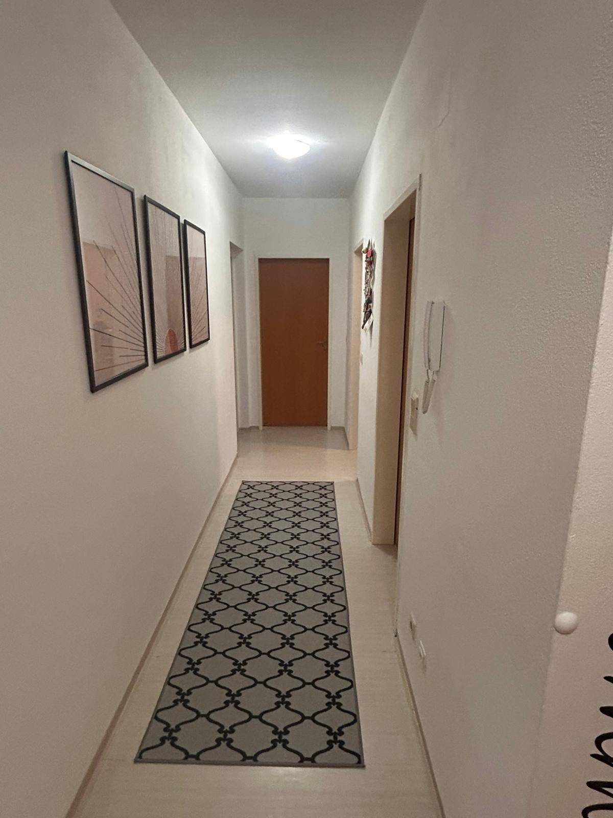 Langer Flur mit dekorativen Bildern an der Wand und einem gemusterten Läufer.