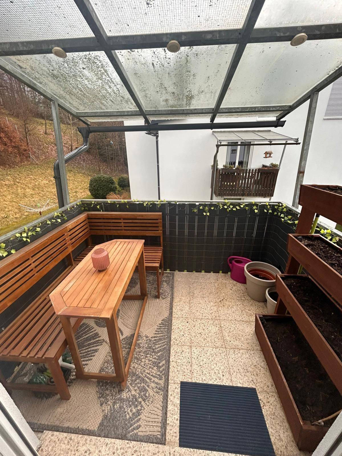 Überdachter Balkon mit Holzsitzgruppe und Hochbeeten, ideal für entspannte Stunden im Freien.