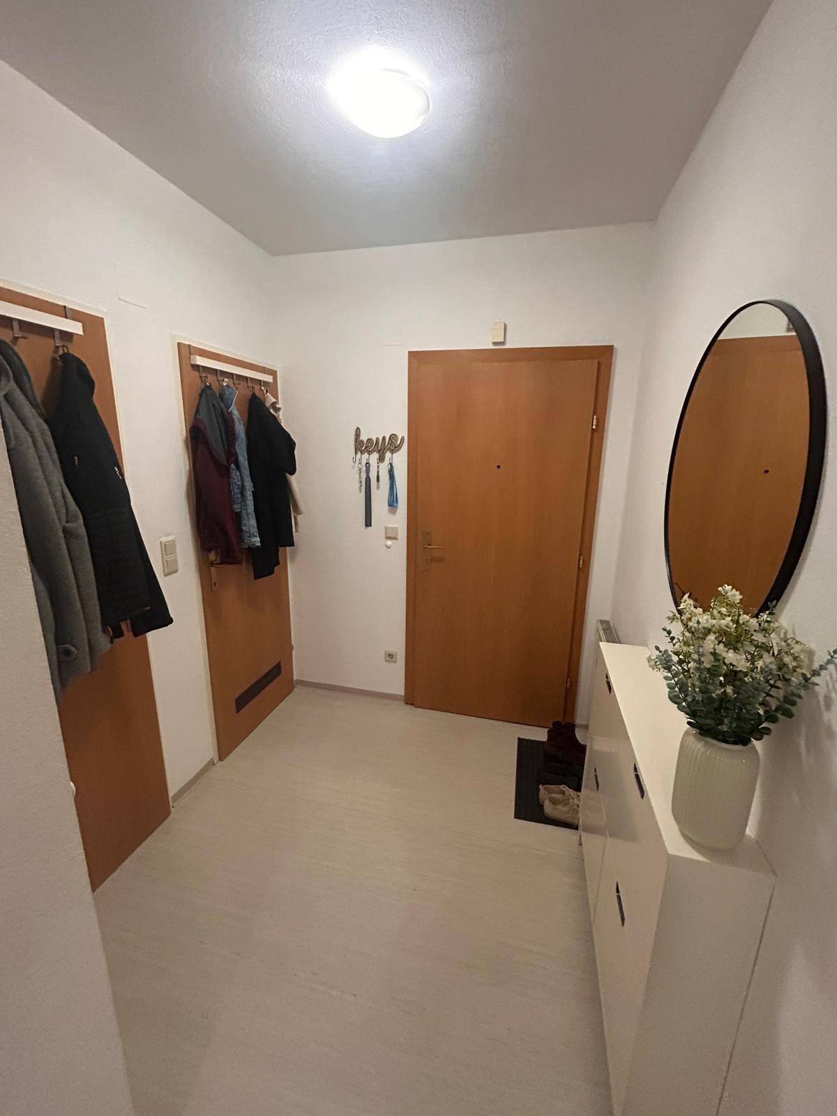 Heller Eingangsbereich mit Garderobe, Spiegel und weißer Kommode für zusätzlichen Stauraum.