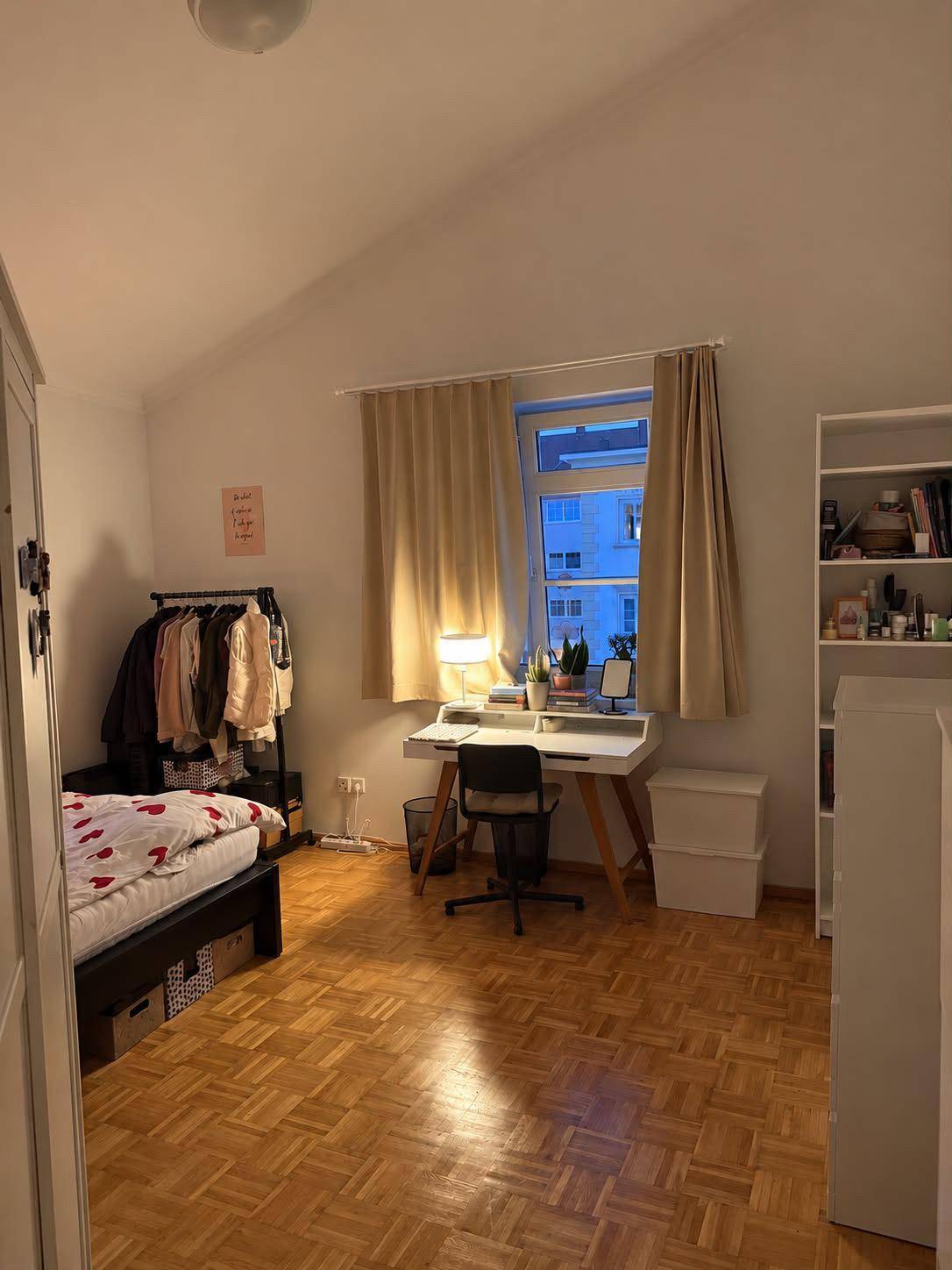 Helles Schlafzimmer mit Parkettboden, Schreibtisch und Kleiderstange unter Dachschräge.
