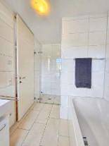 Modernes Badezimmer mit Badewanne, separater Glasdusche und hellen Fliesen an Wänden und Boden.