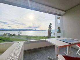 Möblierter Balkon mit Glasbrüstung und weitem Blick über den See und die Berge.