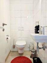 Kleines Gäste-WC mit wandhängender Toilette, Waschbecken und weißen Wandfliesen.
